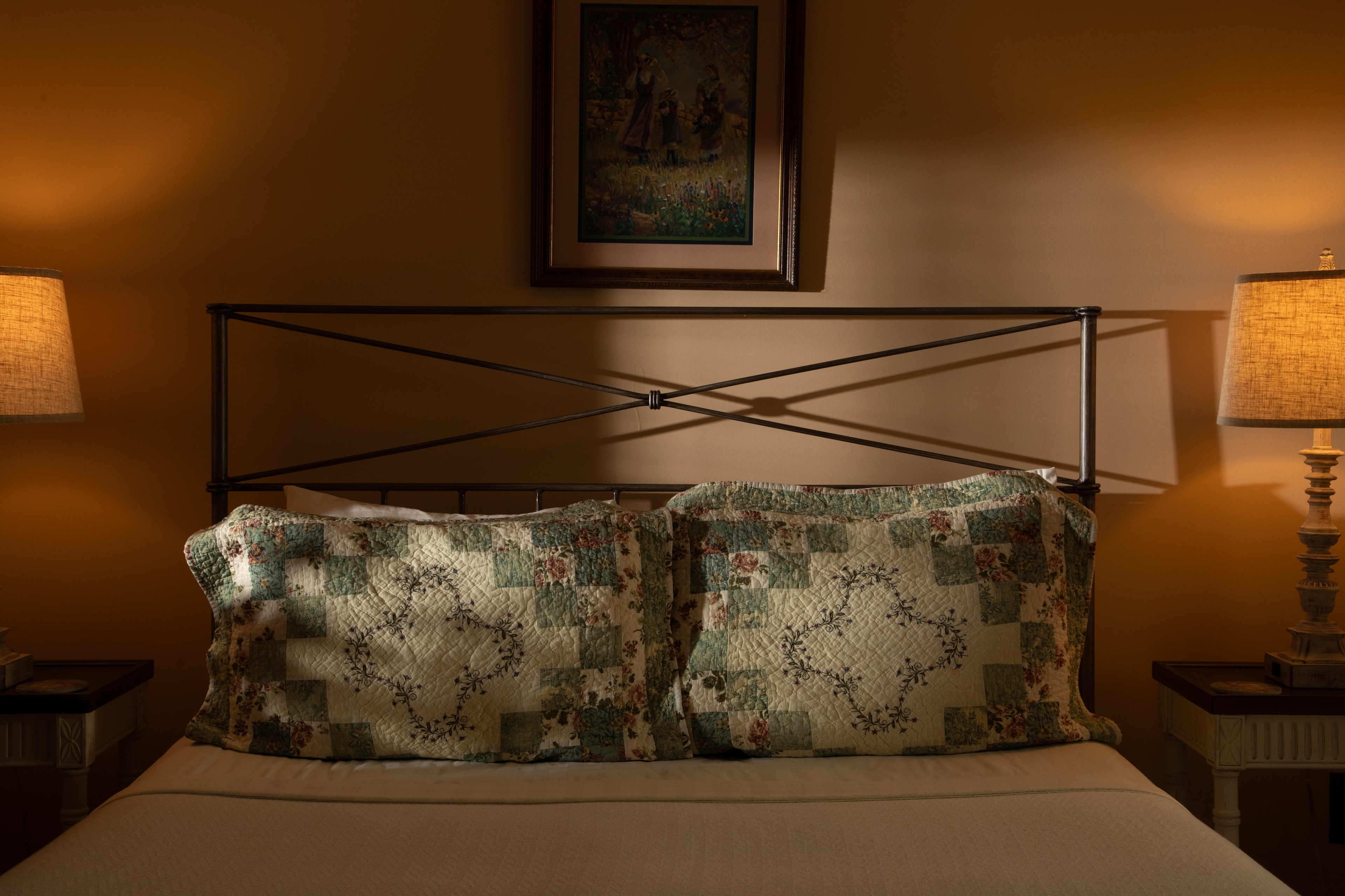 A cozy bed with decorative quilted pillows, illuminated by soft lamp light.