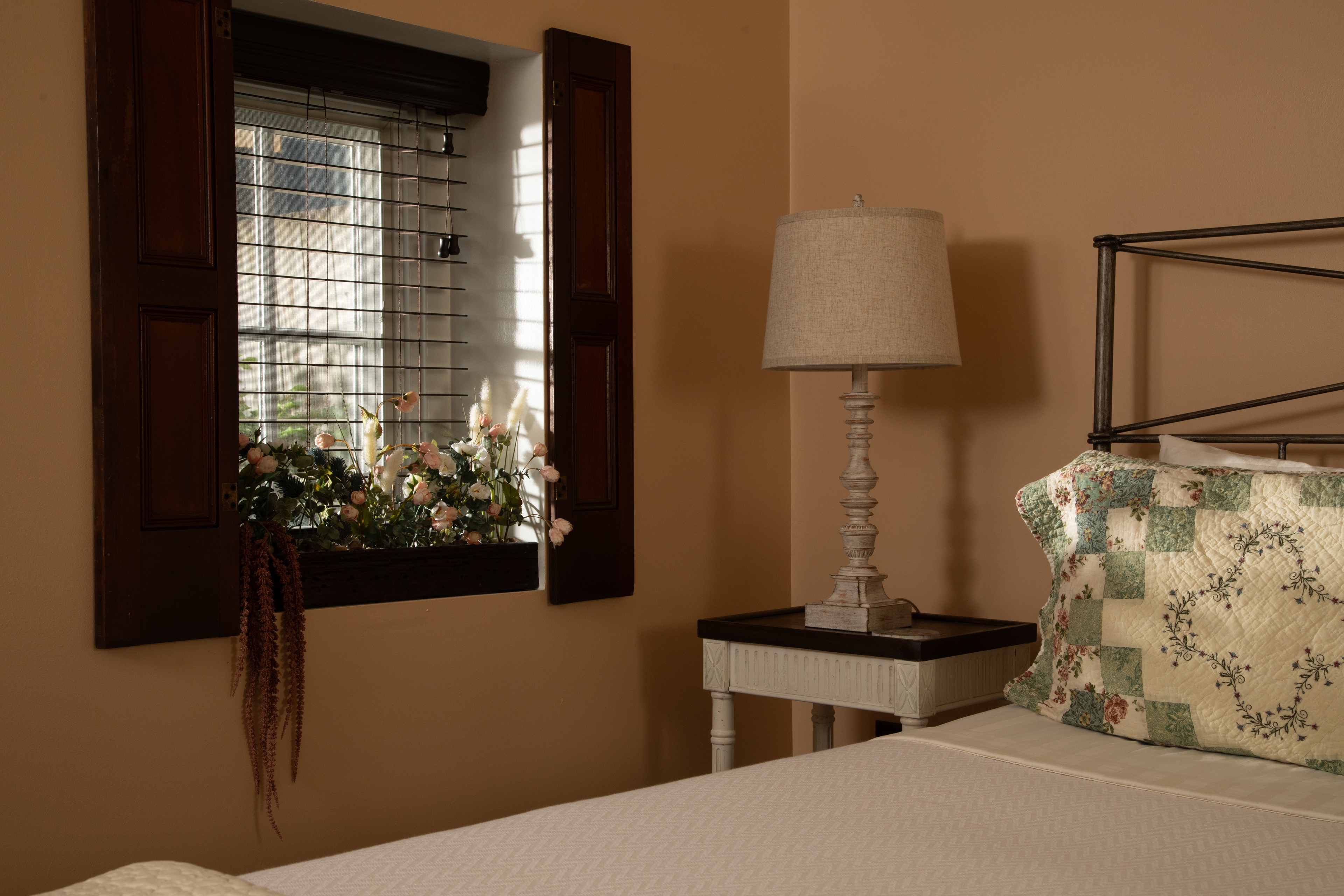 A cozy bedroom corner featuring a lamp, a quilted pillow, and a floral window box.