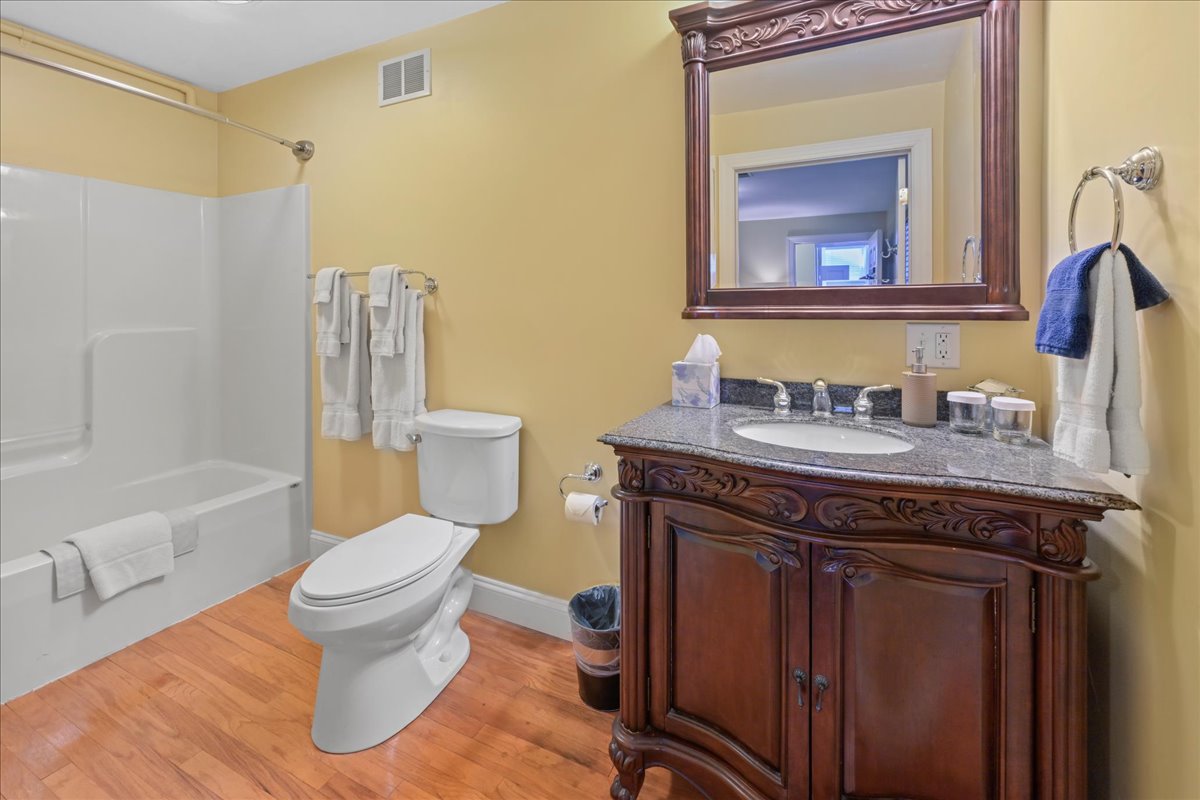The Longstreet Chamber bathroom features wooden floors, an ornate wooden sink cabinet with marble top, toilet, and a tub / shower
