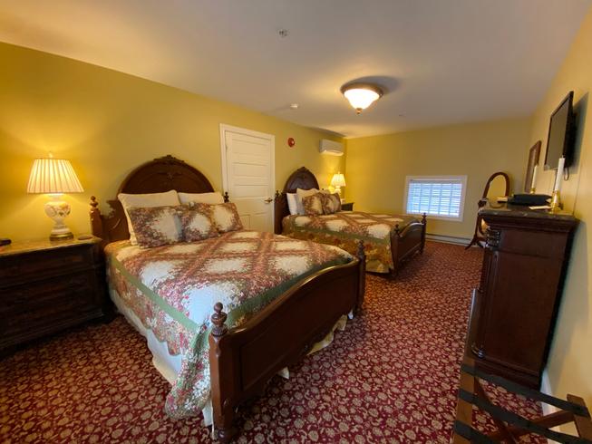 The Swope Suite with two queen-size beds, patterned bedspreads, and wooden nightstands flanking the beds. The walls are light yellow, and the carpet is a red patterned design.
