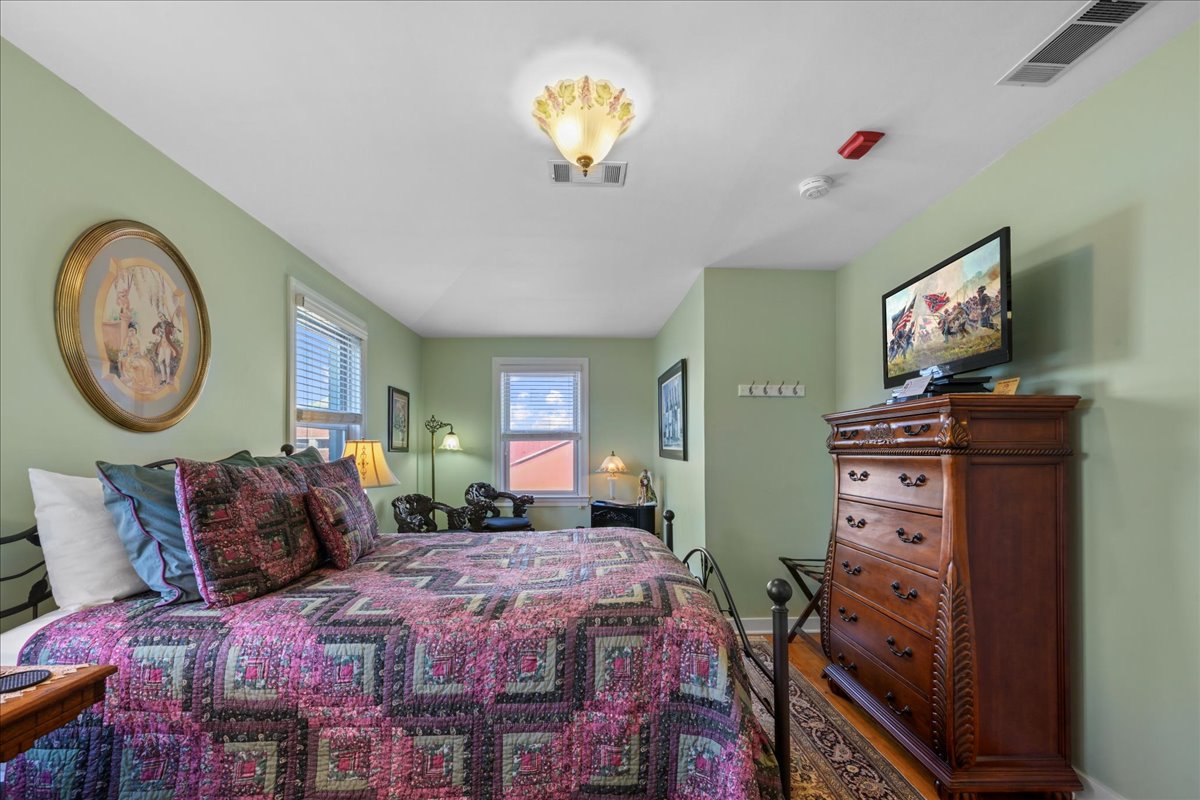 The Cabernet Chamber features a queen-size metal bed, 2 nightstands with lamps, a settee, a dresser, and wooden floors with an area rug.