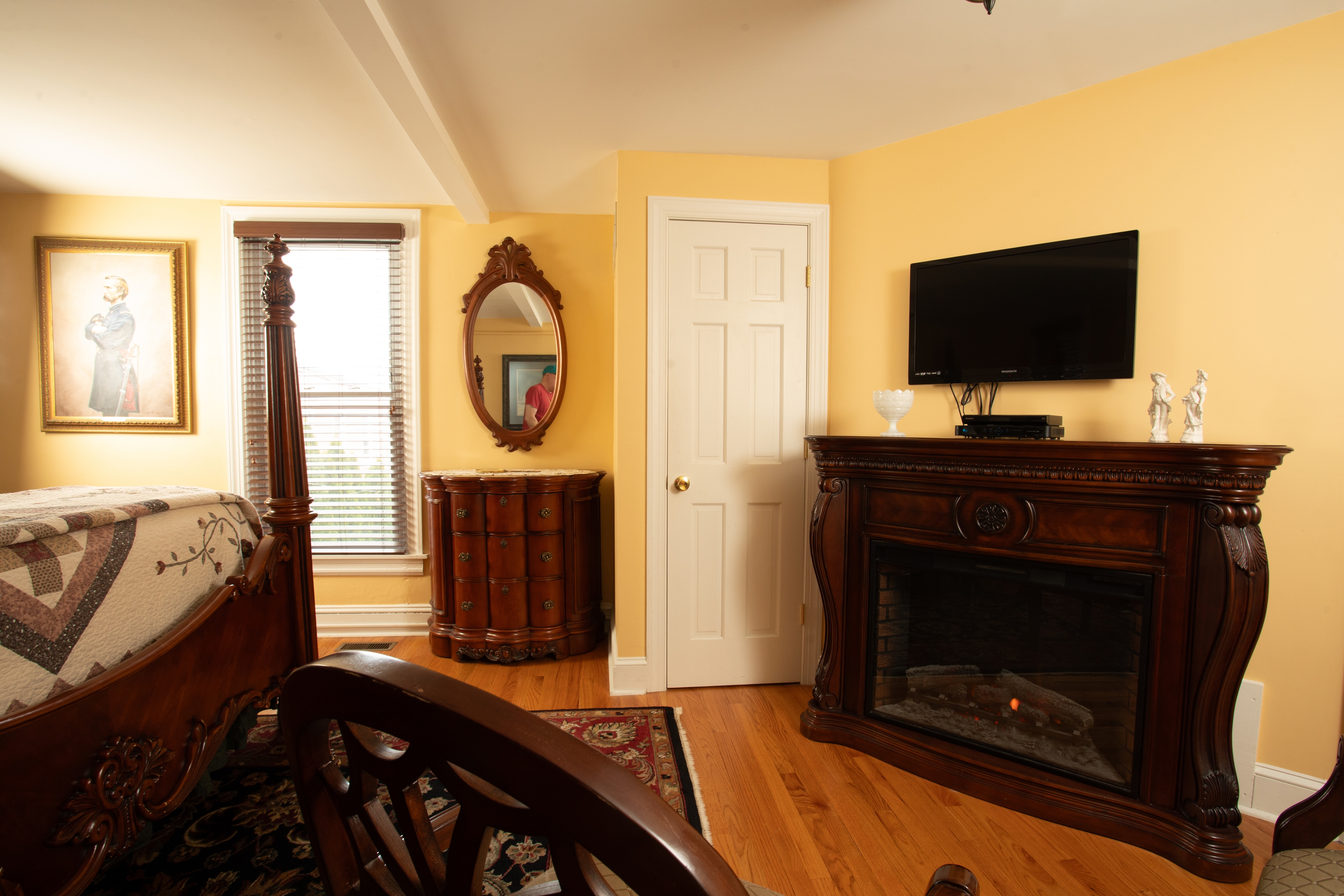The Chamberlain bedroom with a yellow wall, antique furniture, and a television mounted above a fireplace.