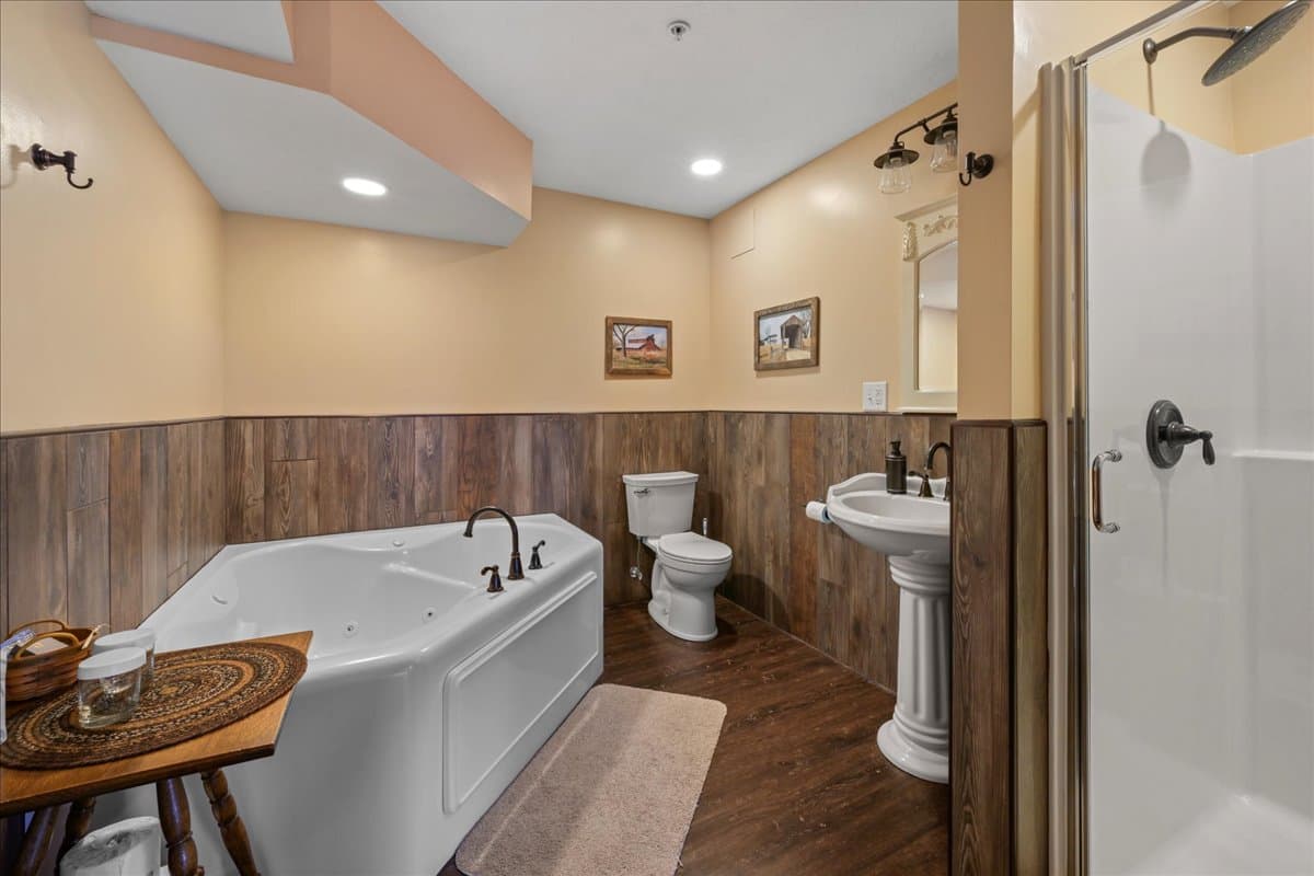 The Carriage House bathroom includes a pedestal sink, jetted tub, toilet, and a walk in shower.