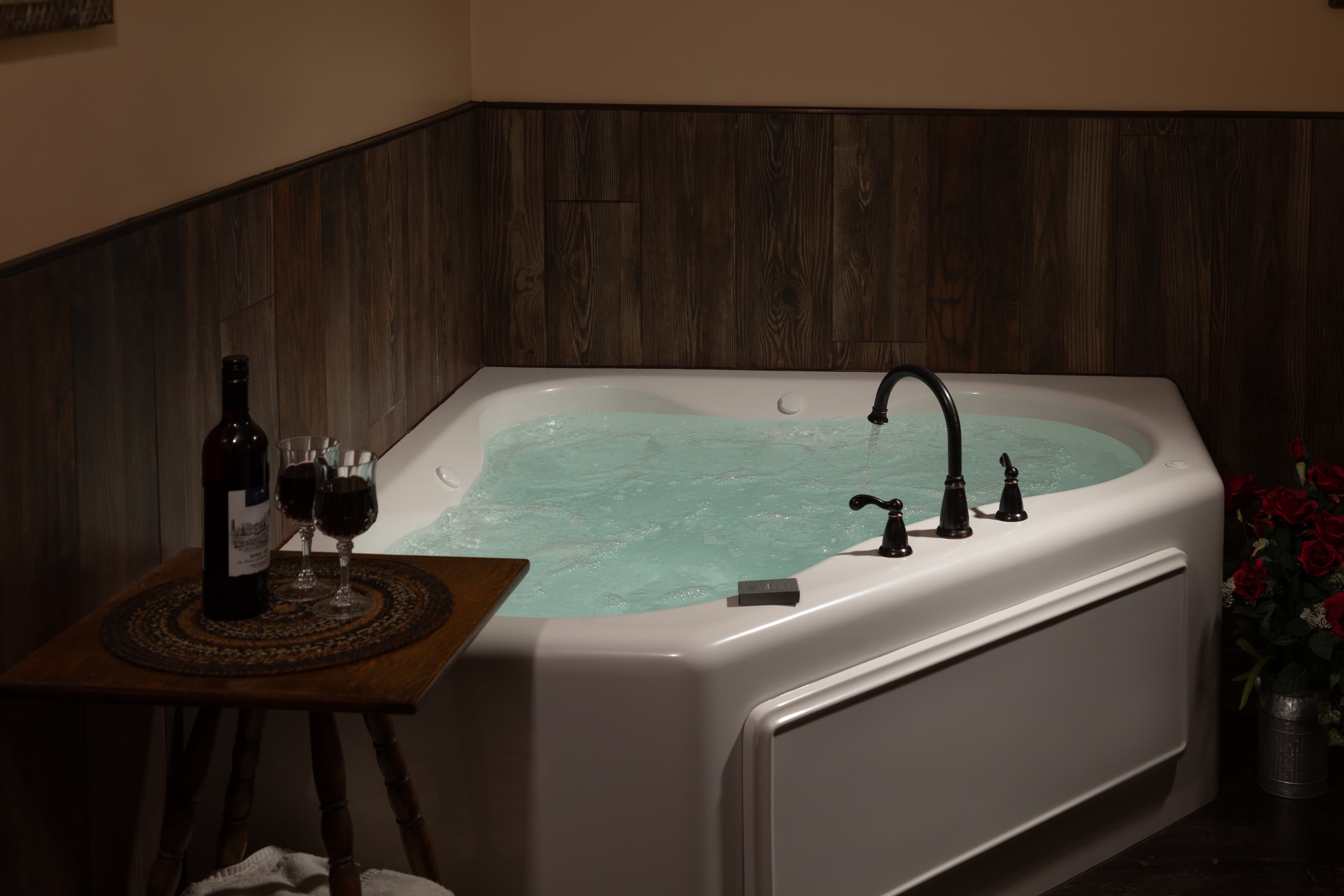 A cozy corner in the Carriage House featuring a heart-shaped hot tub next to a bottle of wine and two glasses.