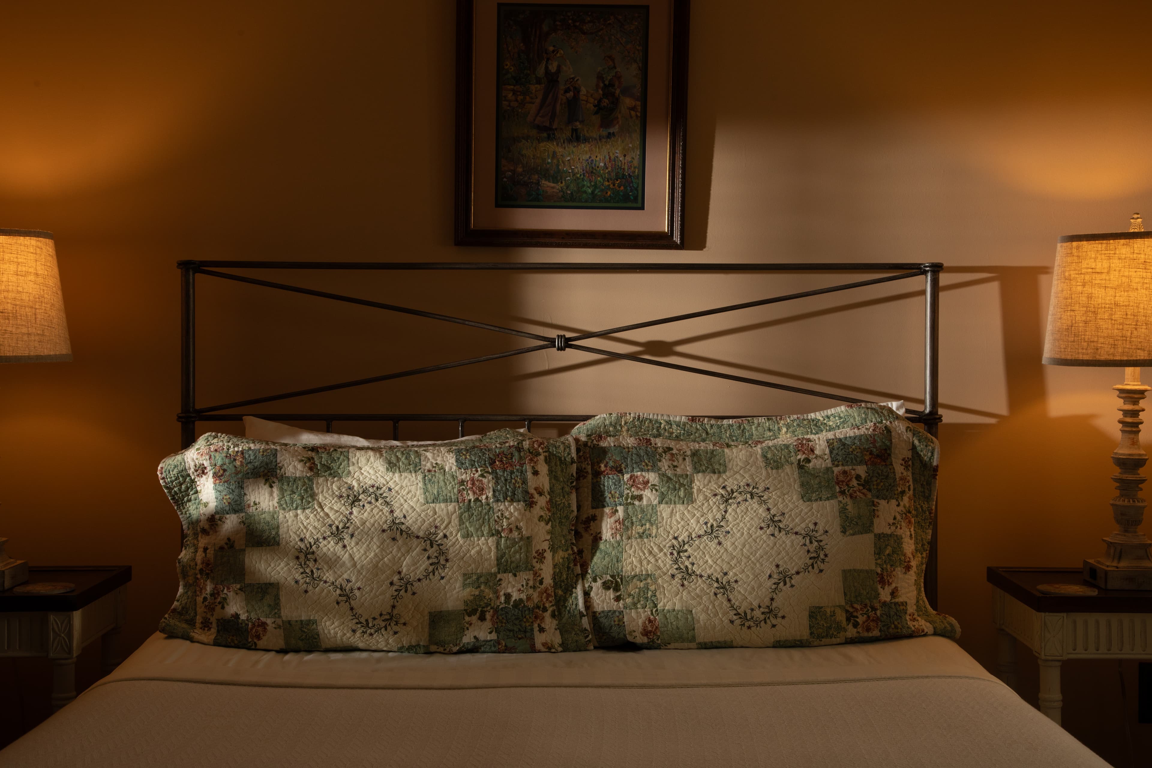 A cozy bed with decorative quilted pillows, illuminated by soft lamp light.