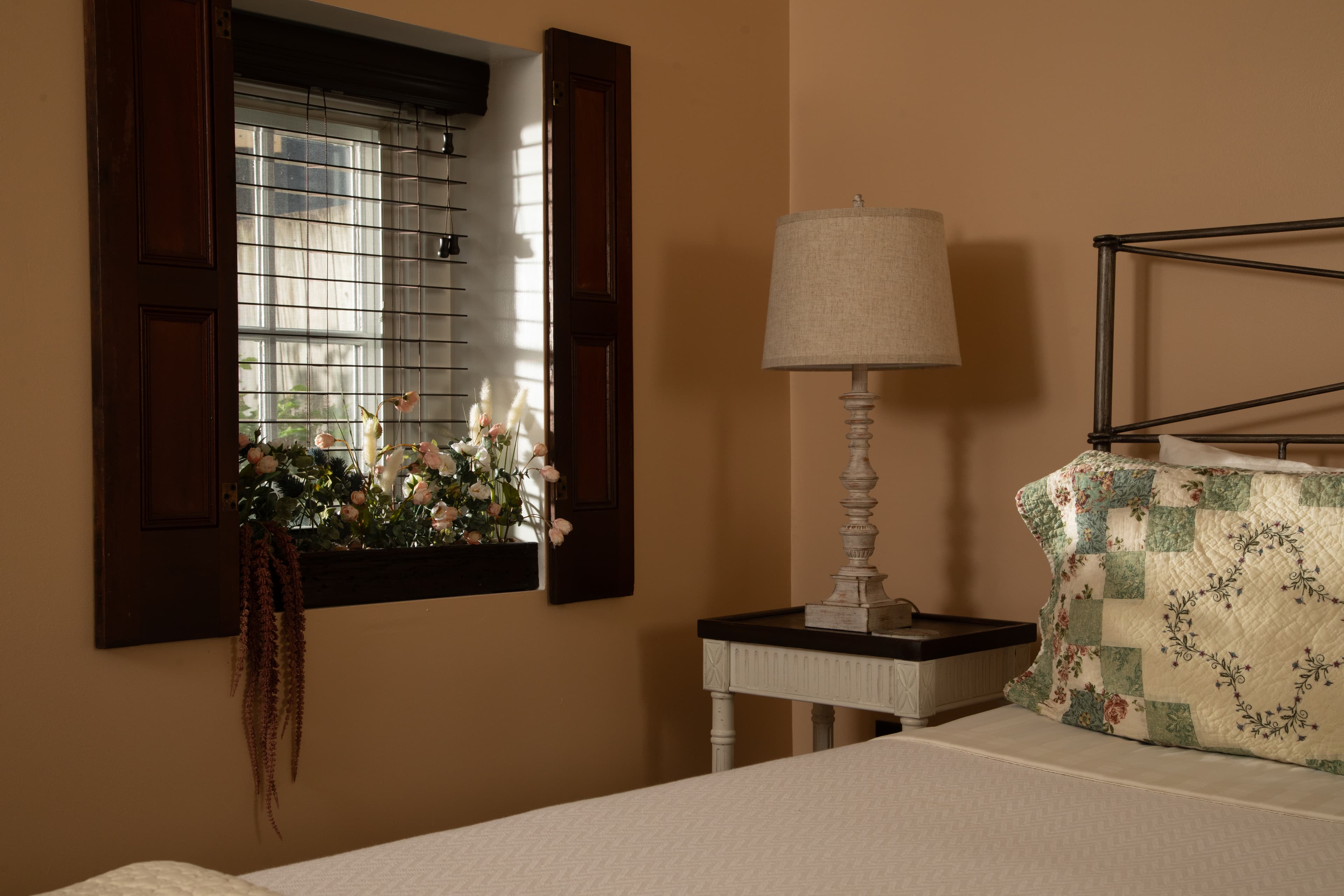 A cozy bedroom corner featuring a lamp, a quilted pillow, and a floral window box.