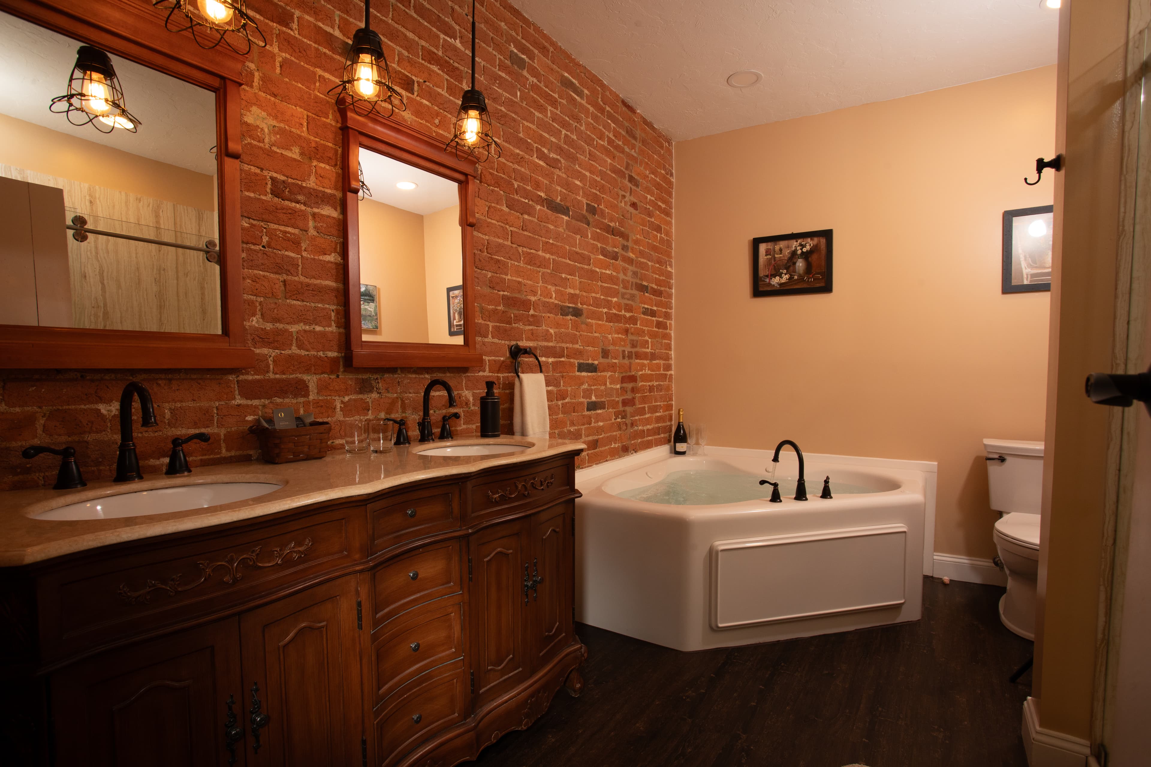 A cozy bathroom featuring a brick wall, double vanity with mirrors, a freestanding bathtub, and warm lighting.