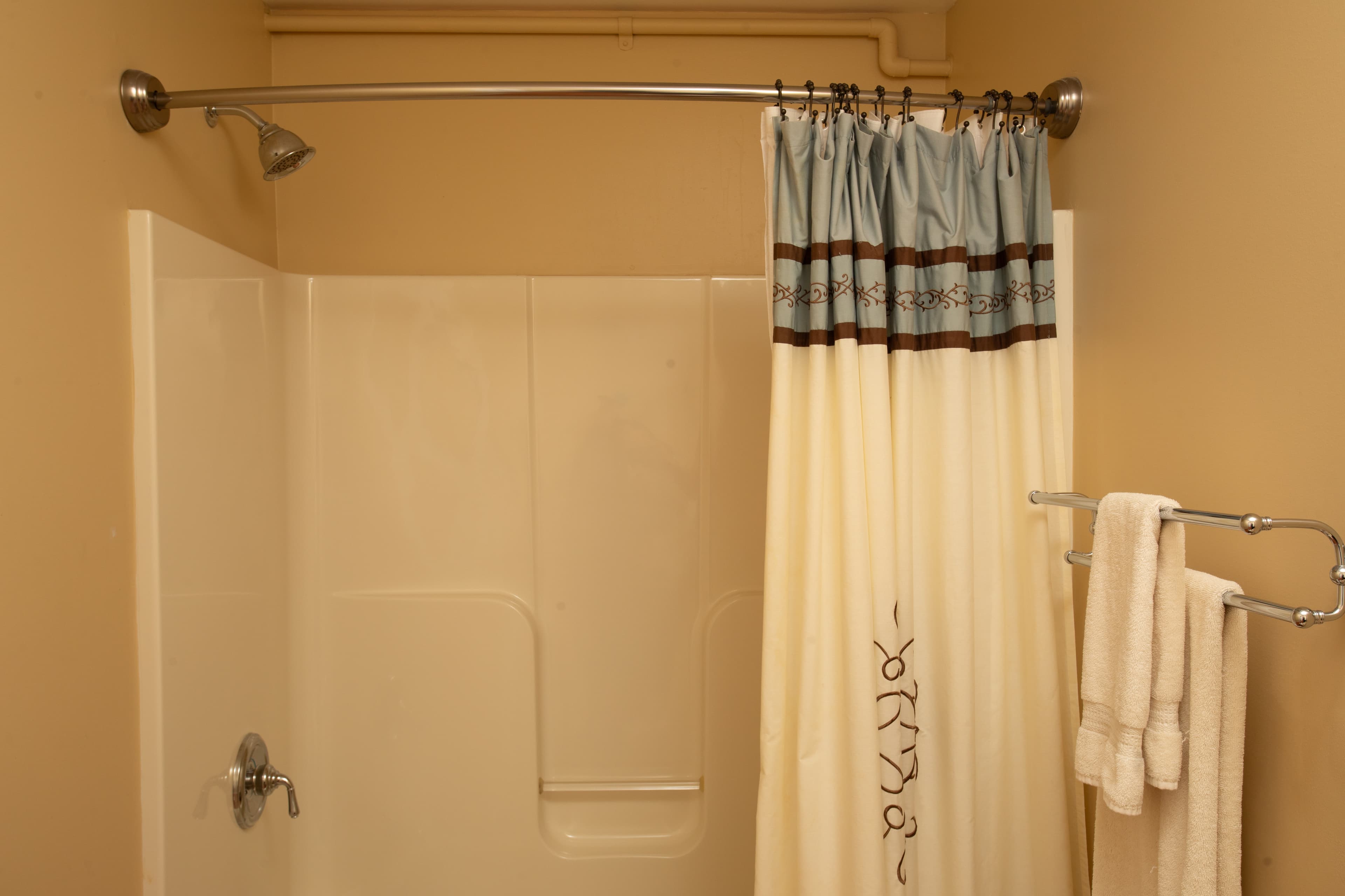 A clean bathroom shower with a shower curtain, towel rack, and folded towels.