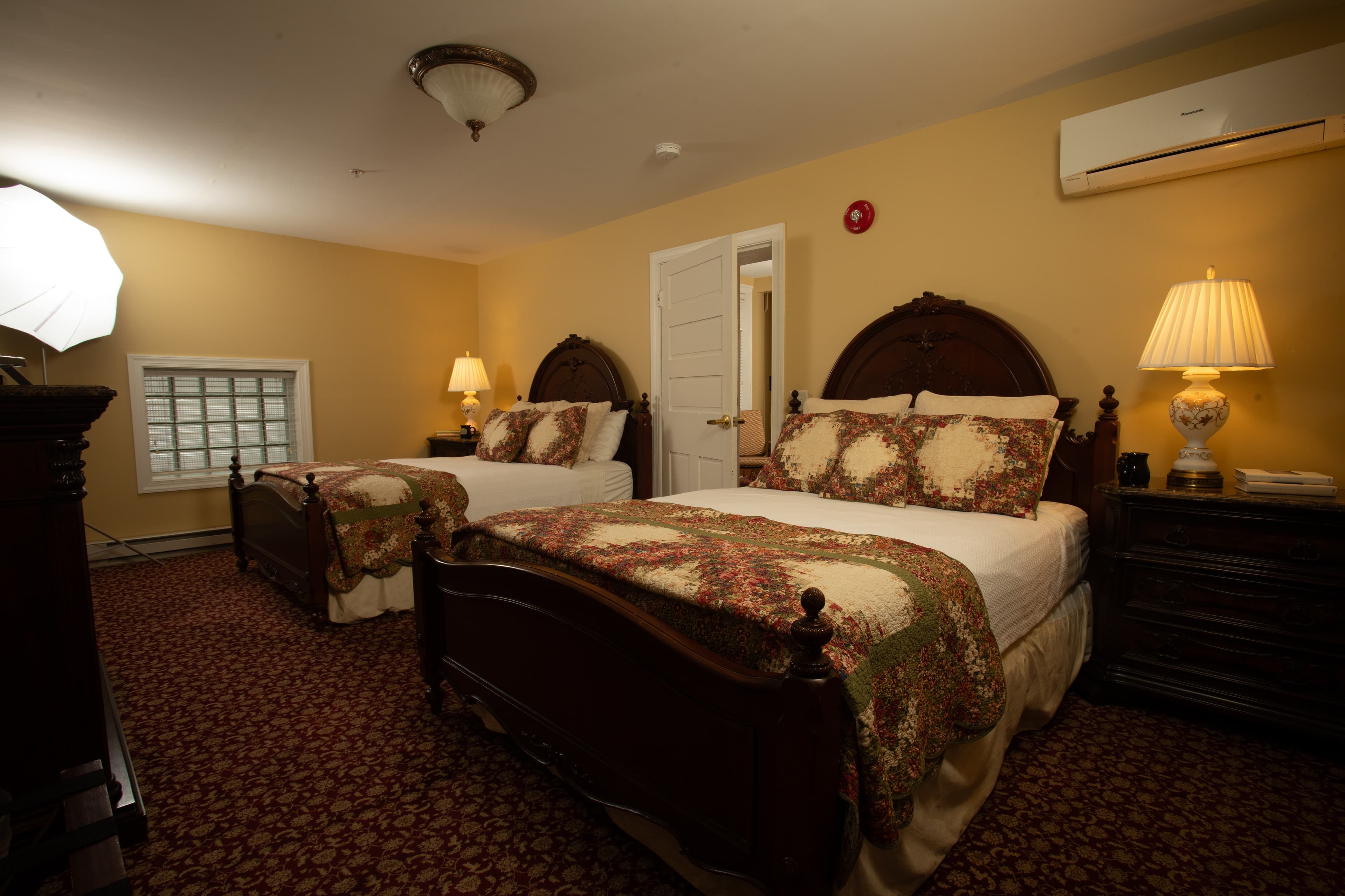 A cozy guest room featuring two wooden beds with ornate headboards, decorative quilts, and warm lighting.