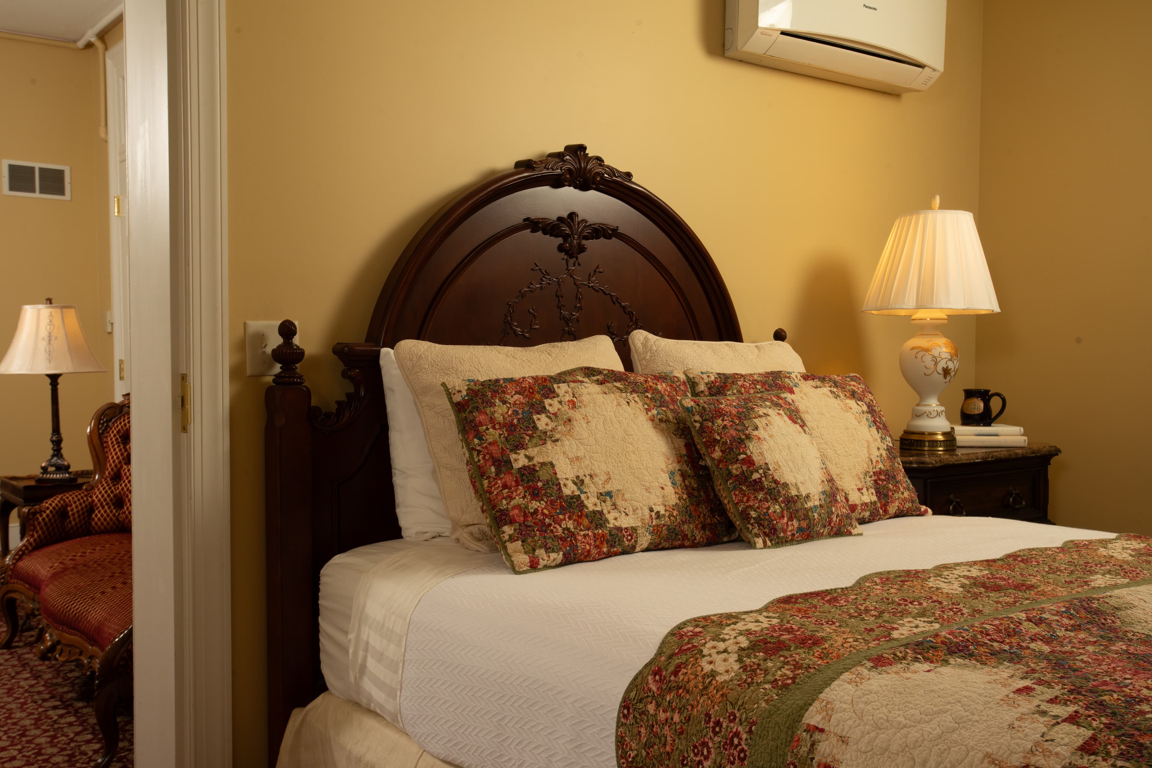 A cozy bedroom featuring a wooden bed with decorative pillows, a quilt, and softly lit lamps.