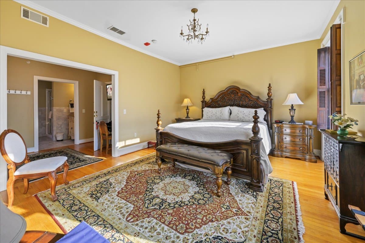 The Miss Dorothy Suite features a Grand King size wooden bed with a  white quilted covering.  This room also has 2 night stands with lamps, a table and 2 chairs in the main bedroom, wooden floors, with area rugs, and an electric fireplace.