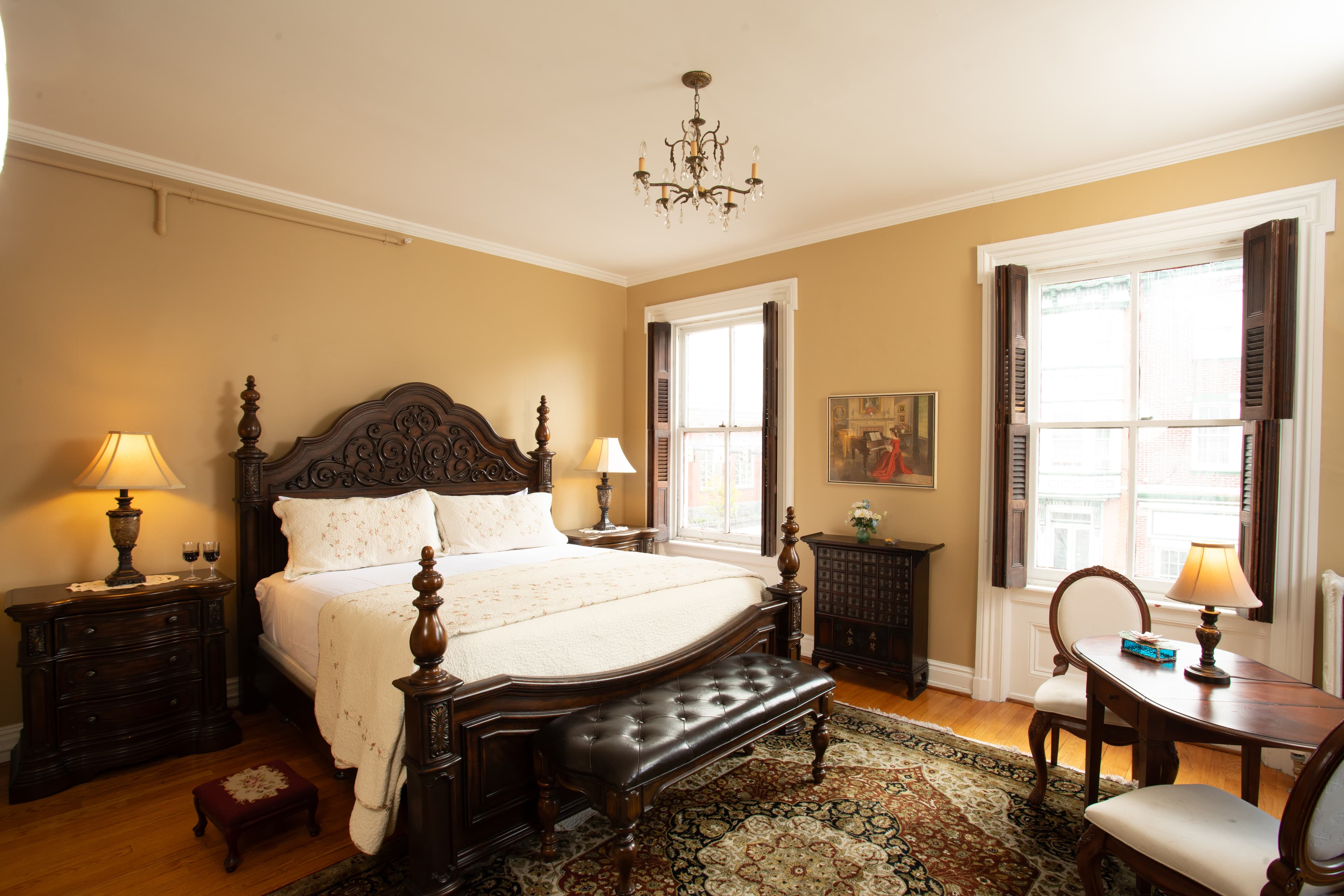 Elegant bedroom featuring a king-size bed, antique furniture, and natural light from large windows.