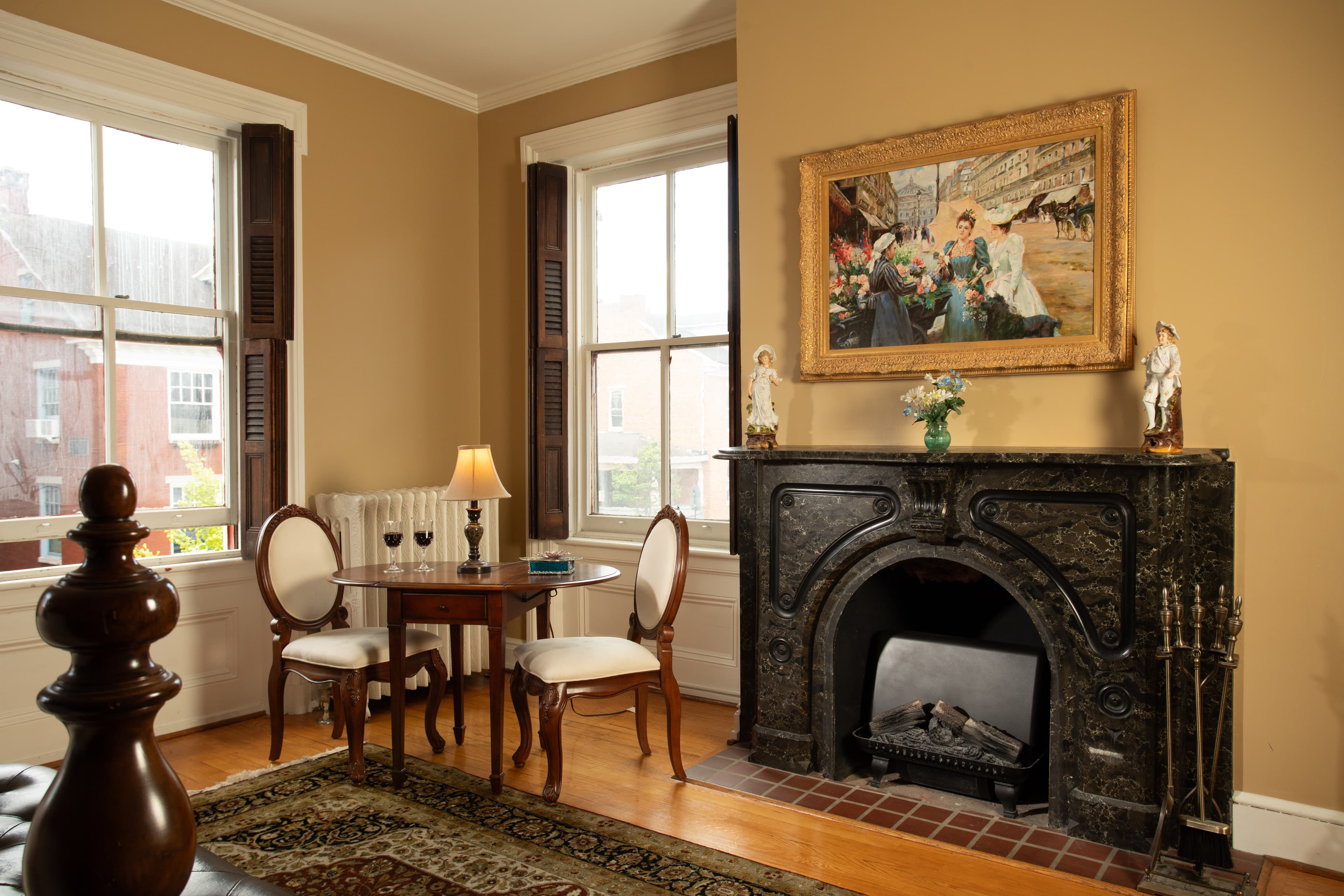 A cozy living space featuring a small dining table, two chairs, a fireplace, and a framed painting on the wall.