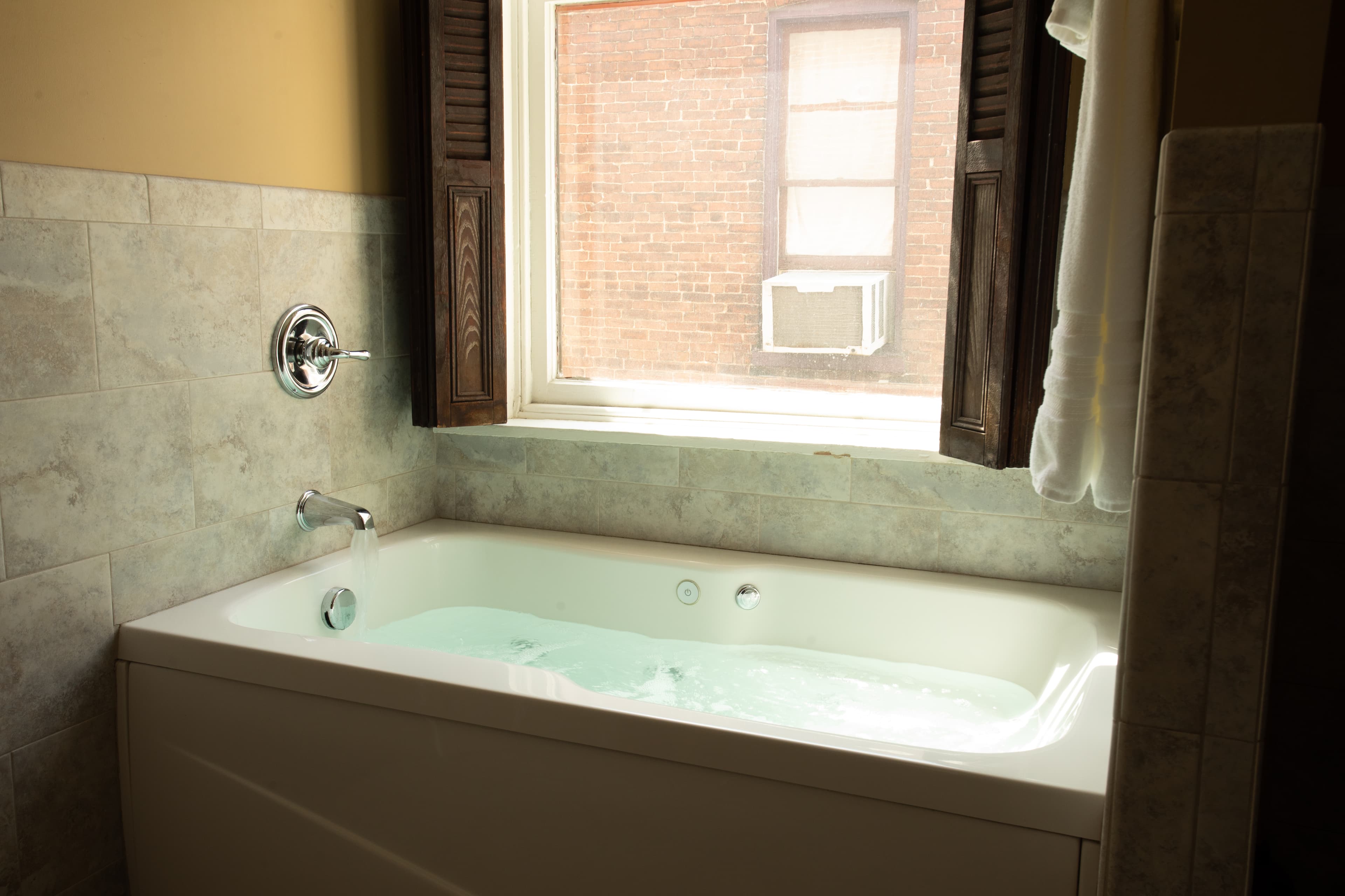 A bright bathroom featuring a spacious tub with water and a window with wooden shutters.