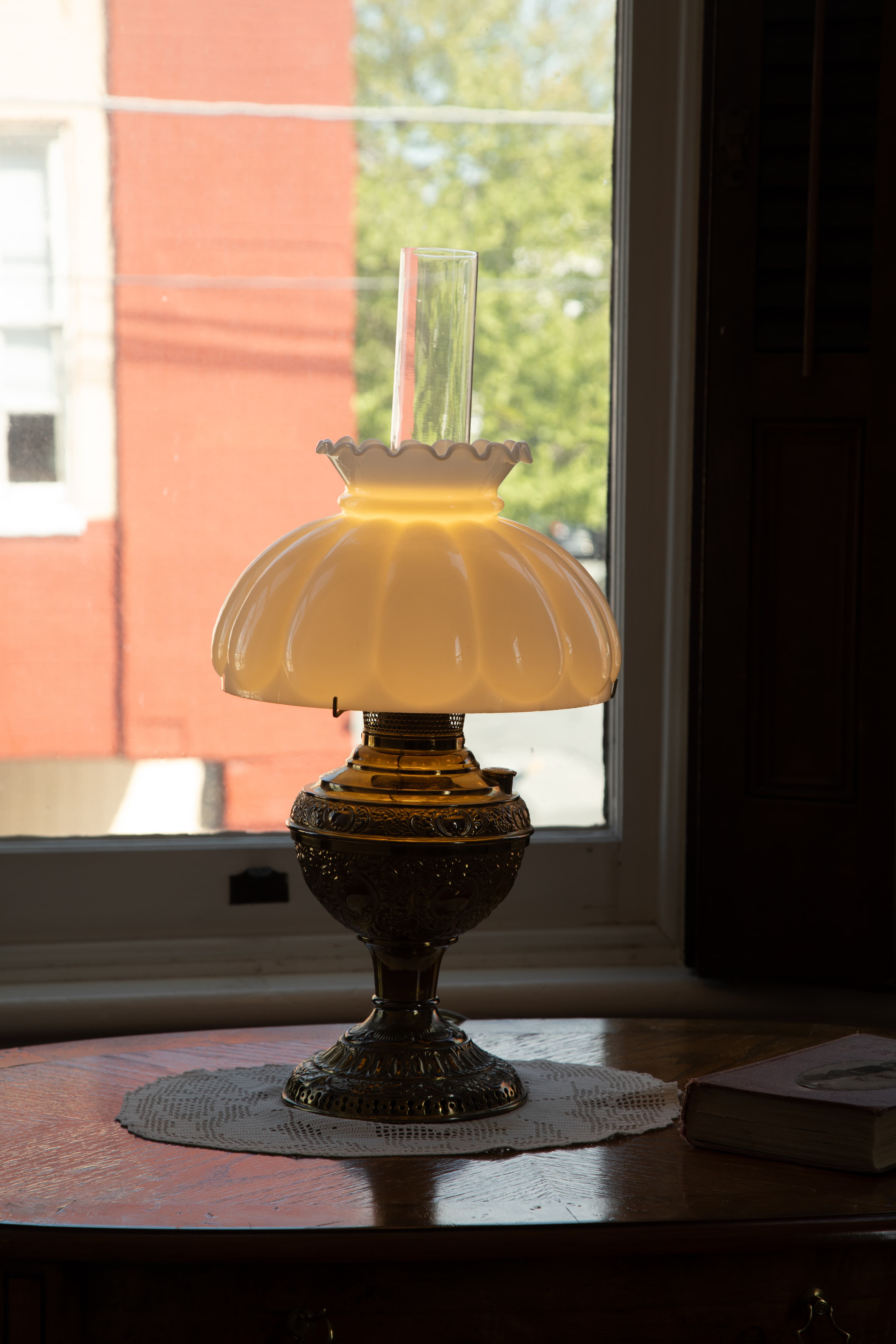 A vintage lamp with a frosted glass shade sits on a table near a window.