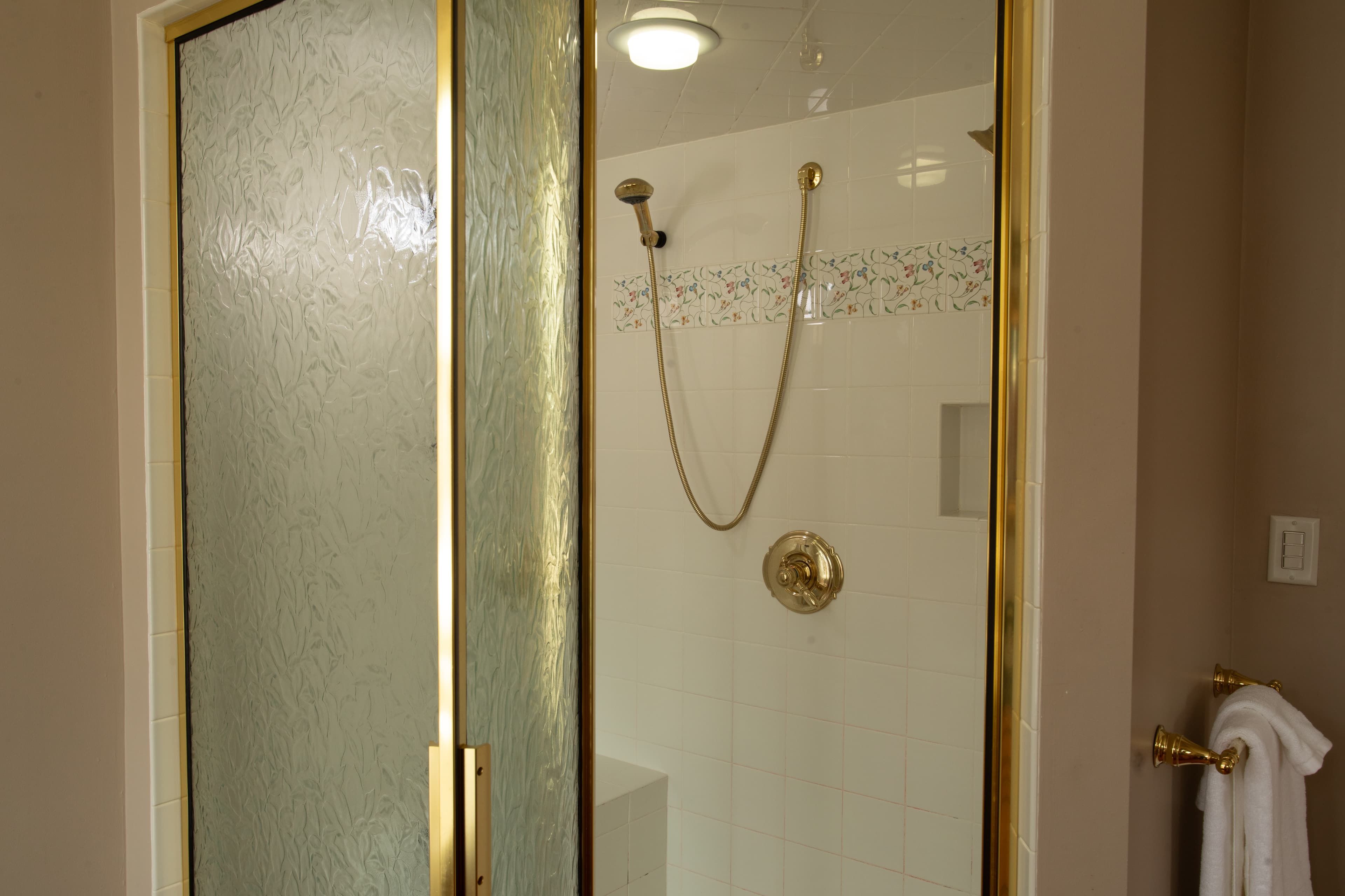 A bathroom shower with glass doors and gold fixtures.