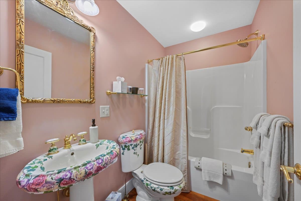 The Miss Emily Rose Chamber bathroom features ornate Italian pedestal sink and toilet, original wooden floors, and a tub / shower combo.