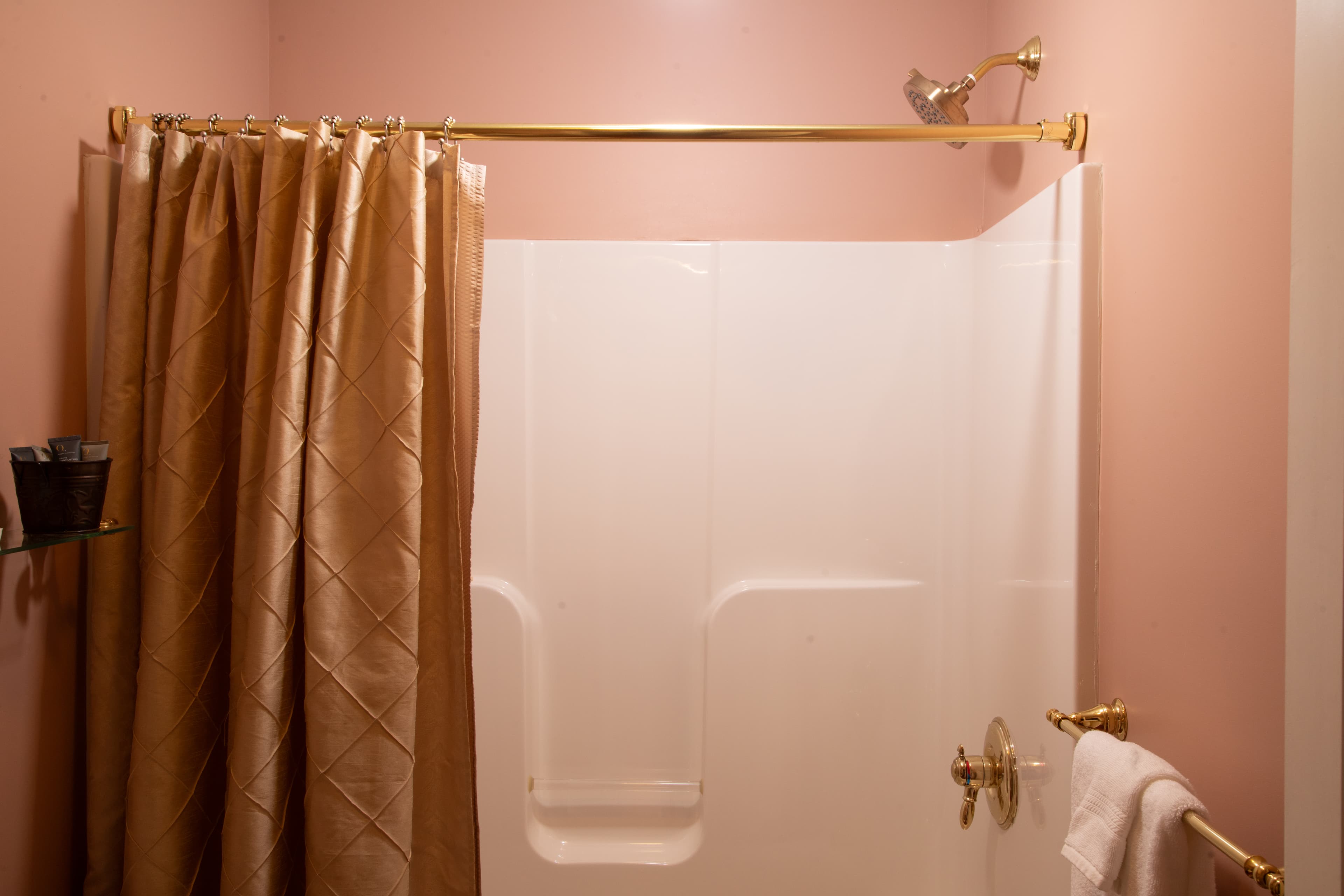 A shower with a gold curtain and fixtures against a pink wall.