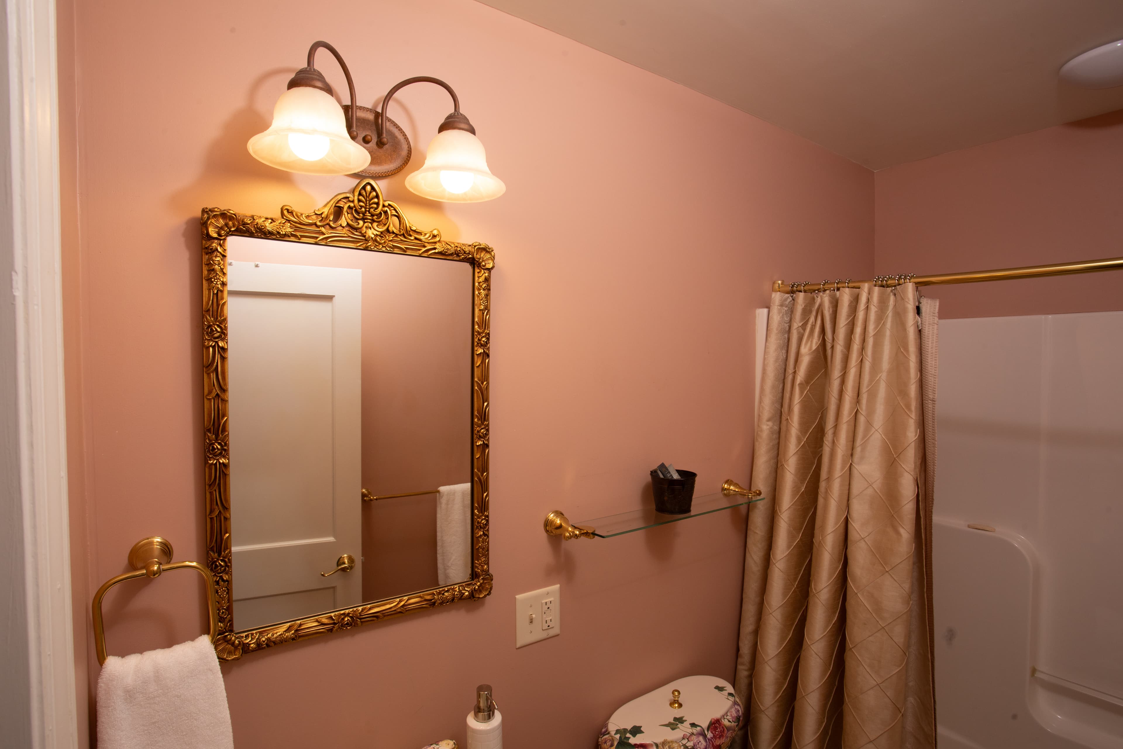 A elegantly styled bathroom with a pink wall, ornate mirror, and decorative lighting.
