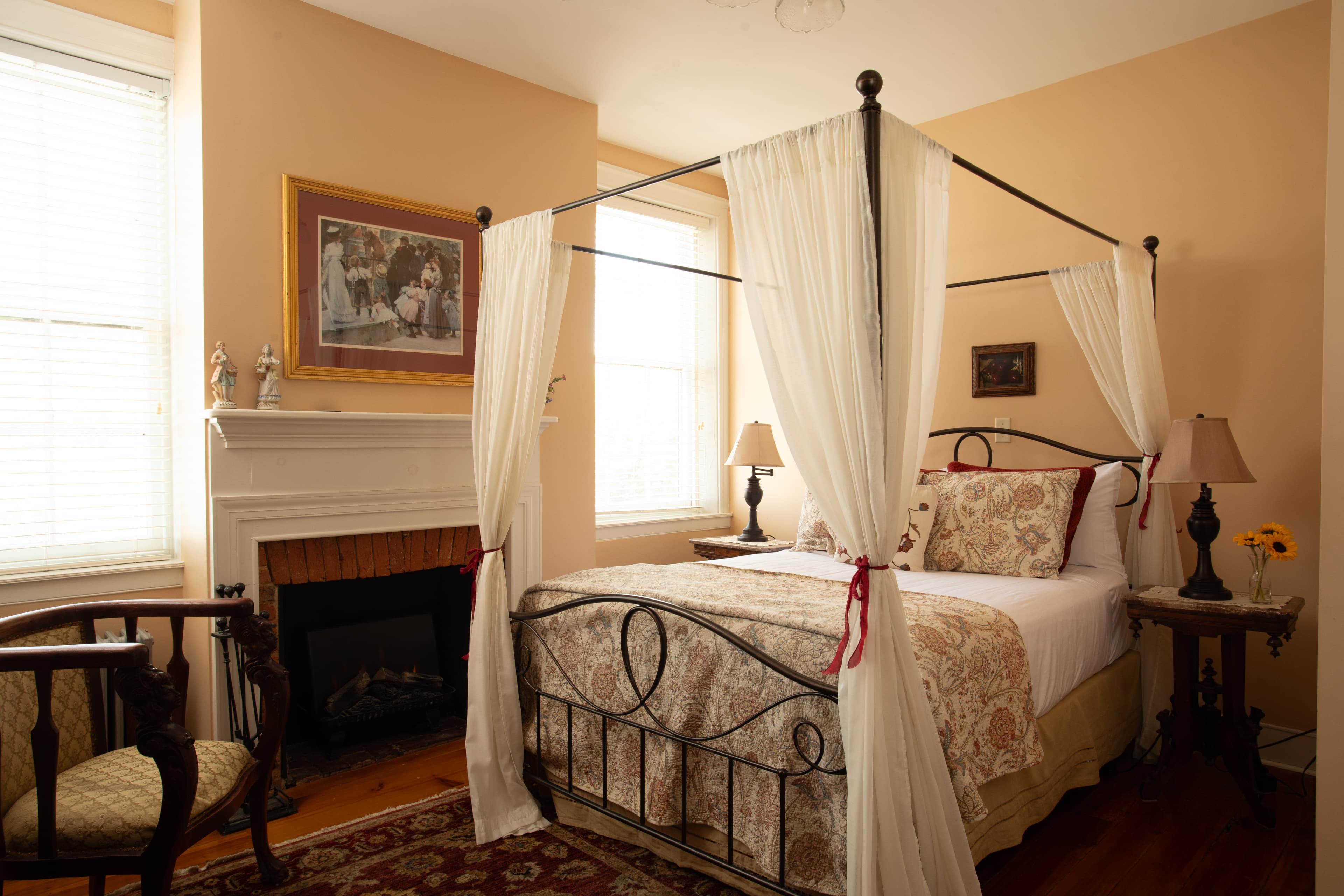 A cozy bedroom featuring a four-poster bed draped with white fabric, a fireplace, and soft lighting.