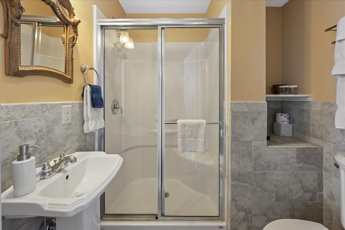 The Norther Spy Chamber bathroom features, a walk-in shower, pedestal sink, toilet, and tile floor.