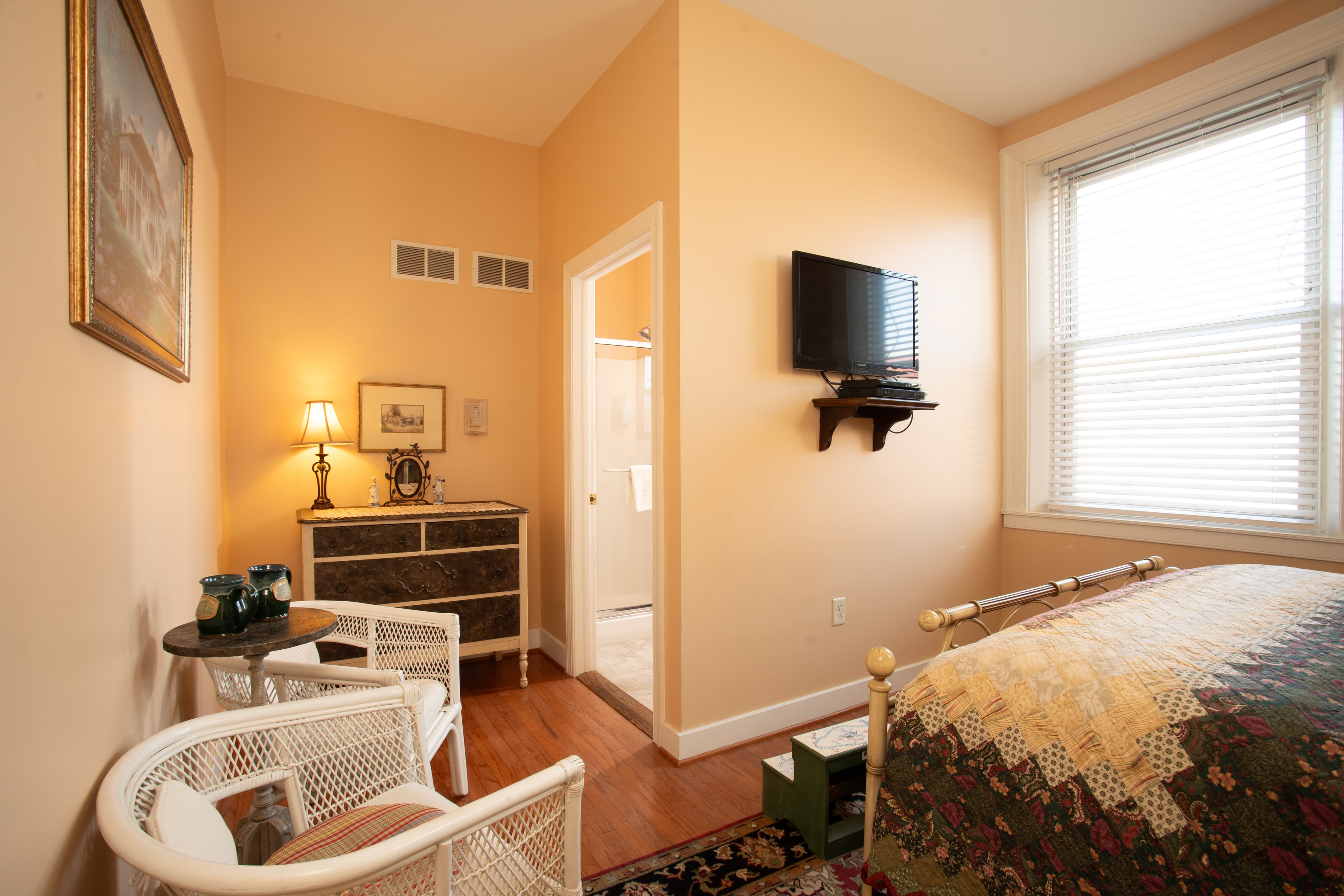 Cozy bedroom featuring a floral bedspread, two chairs, a small TV, and a warm ambiance.