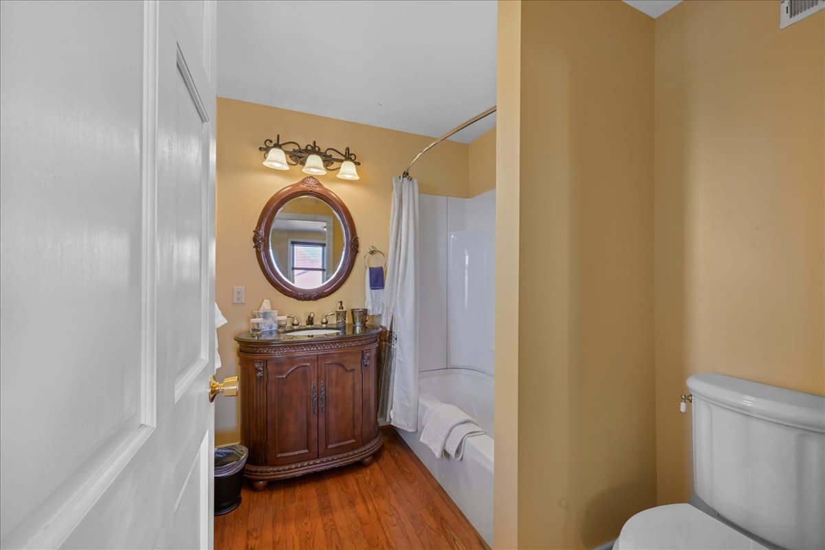Jacob's Den Chamber Bathroom features an ornate wooden vanity/sink, a tub/shower, toilet, and wooden floors.