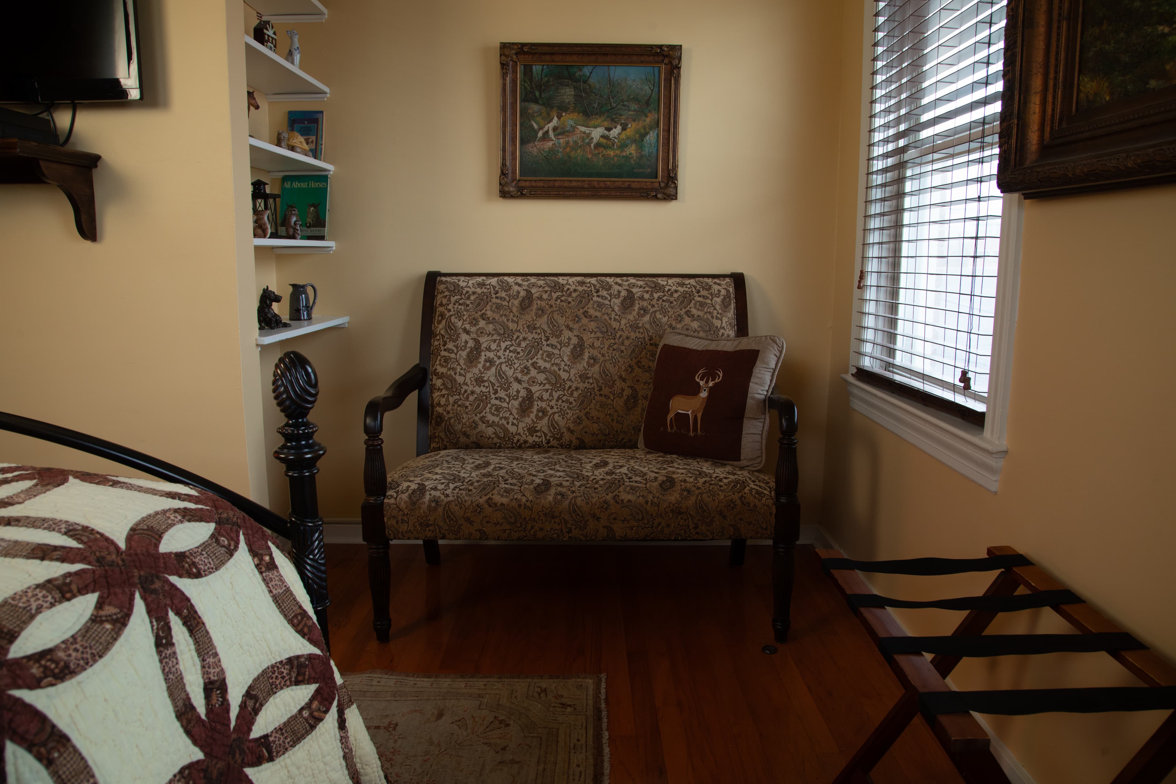 Cozy corner with a patterned loveseat, a decorative pillow, and a wall art piece, illuminated by natural light.