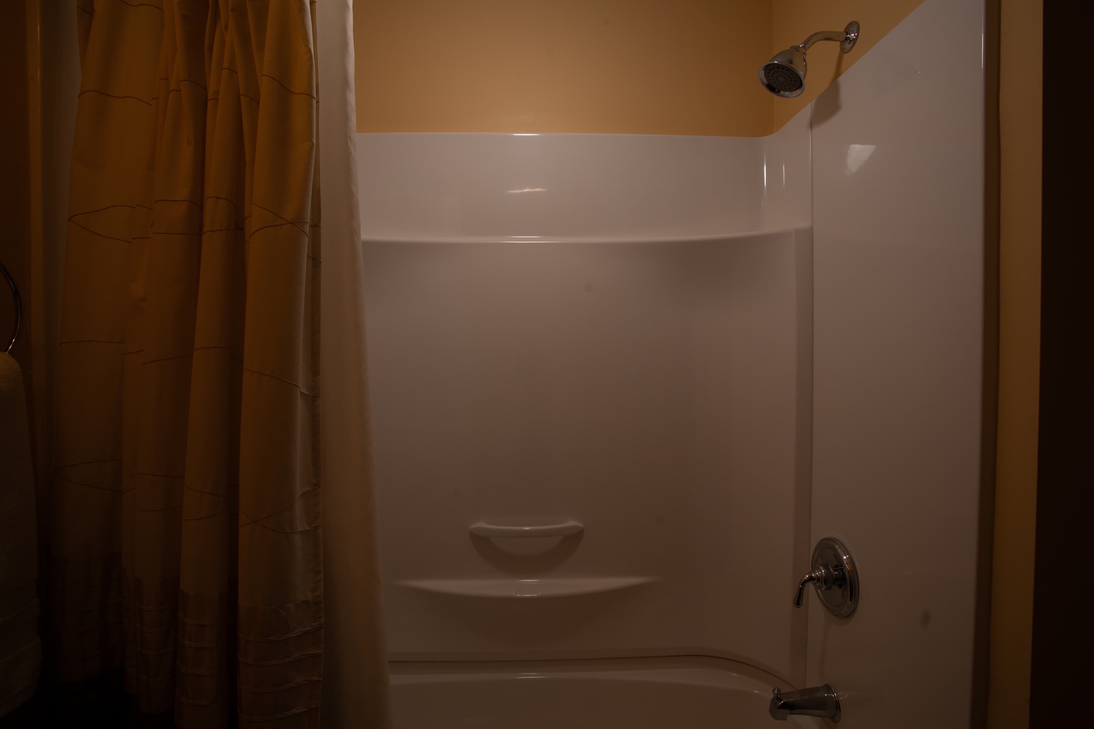 A corner shower stall with a beige curtain and simple fixtures.