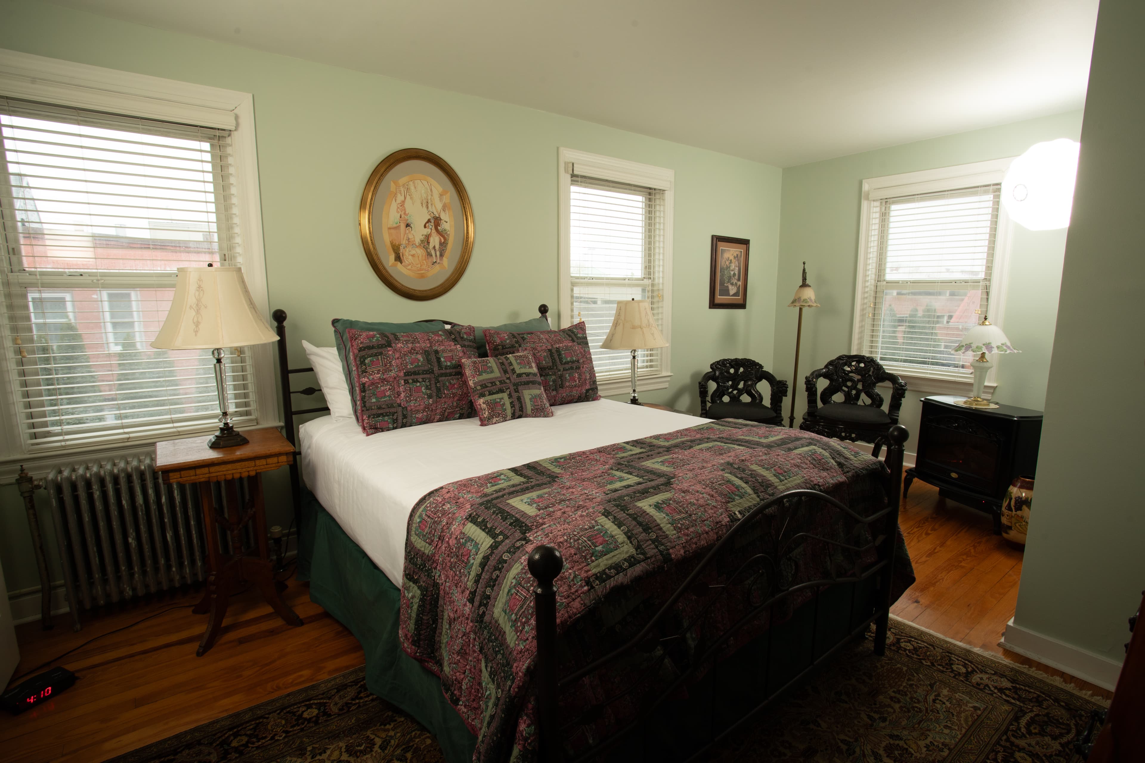 A cozy bedroom, Cabernet Chamber, features a double bed with a patterned quilt, nightstands with lamps, and green walls.