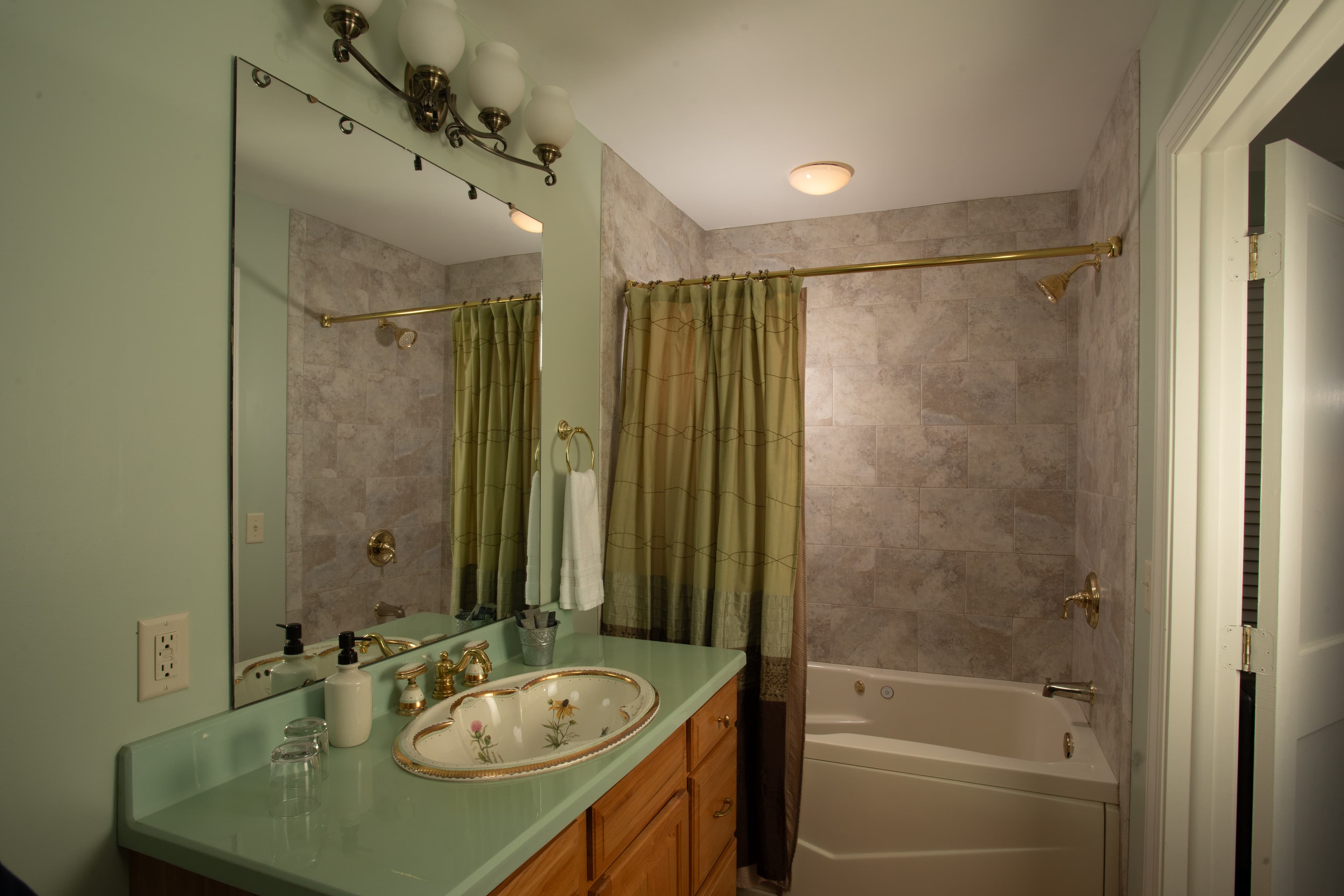The Cabernet Chamber bathroom featuring a green countertop, mirror, and a bathtub with a shower curtain.
