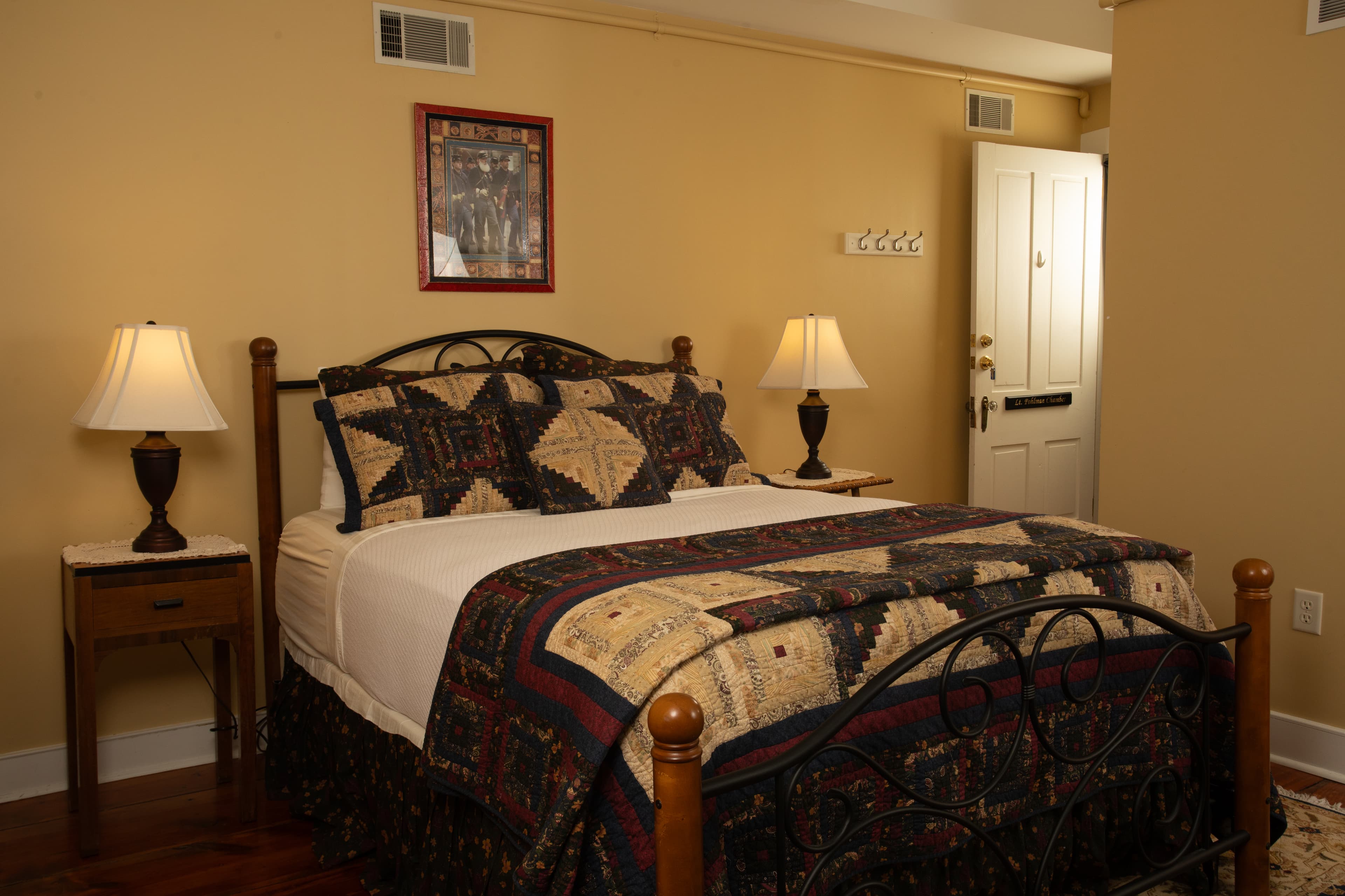 A cozy bedroom featuring a quilted bedspread, two bedside lamps, and a door leading outside.