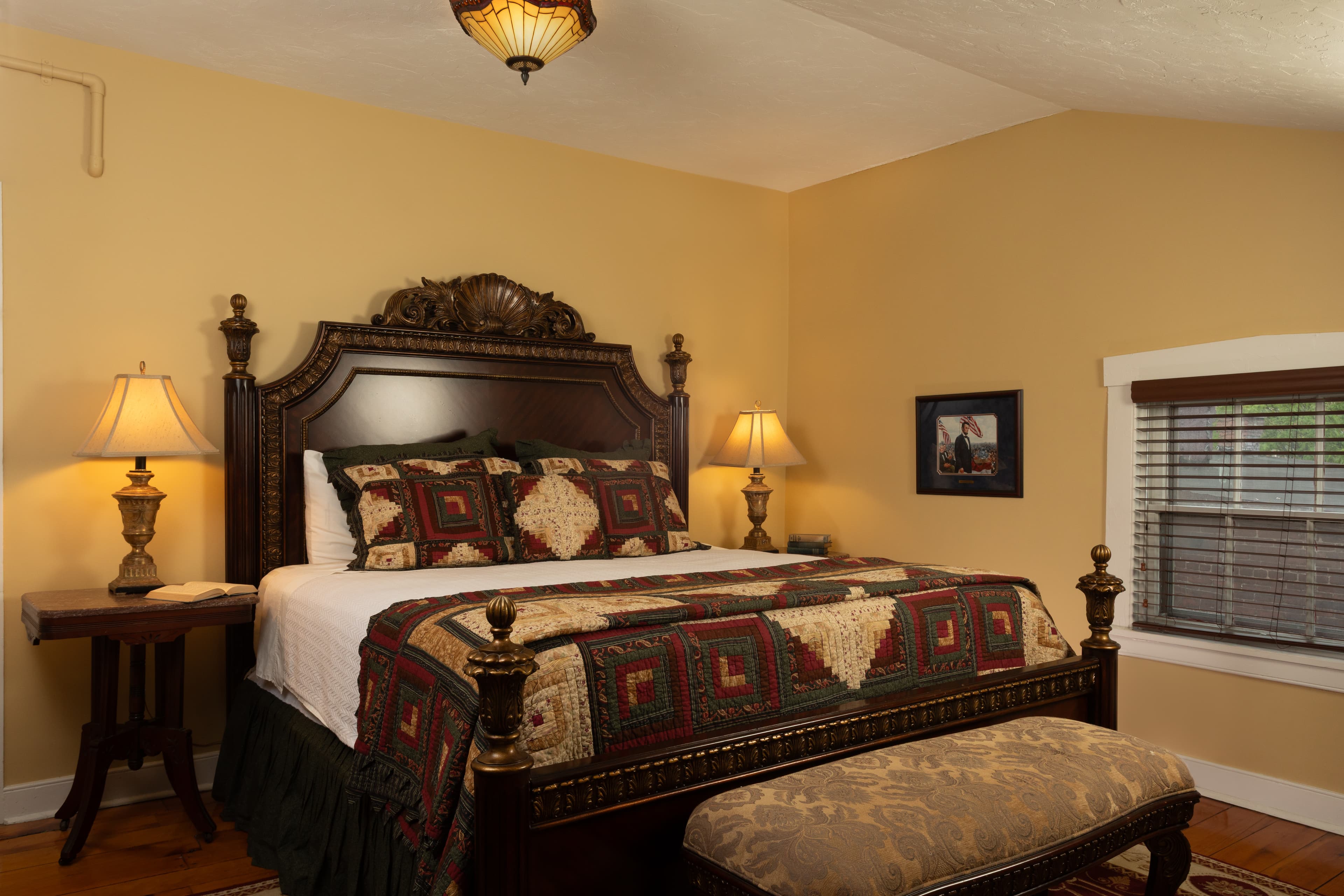 Cozy bedroom featuring a large wooden bed with a patterned quilt, two bedside lamps, and a decorative bench.