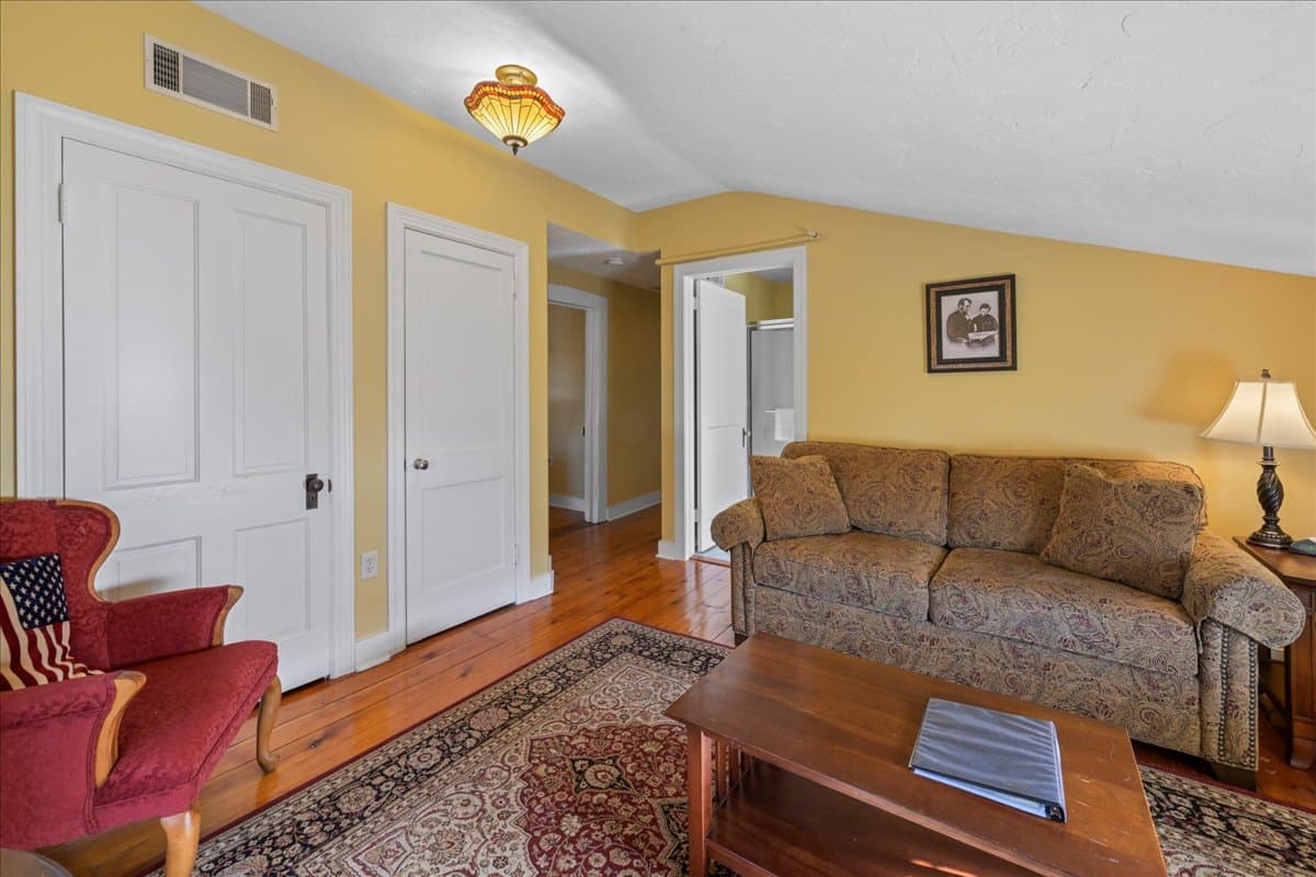 The Lincoln Suite also features a sitting room with a sleeper sofa, a chair, an electric fireplace, TV, and original wooden floors with an area rug.