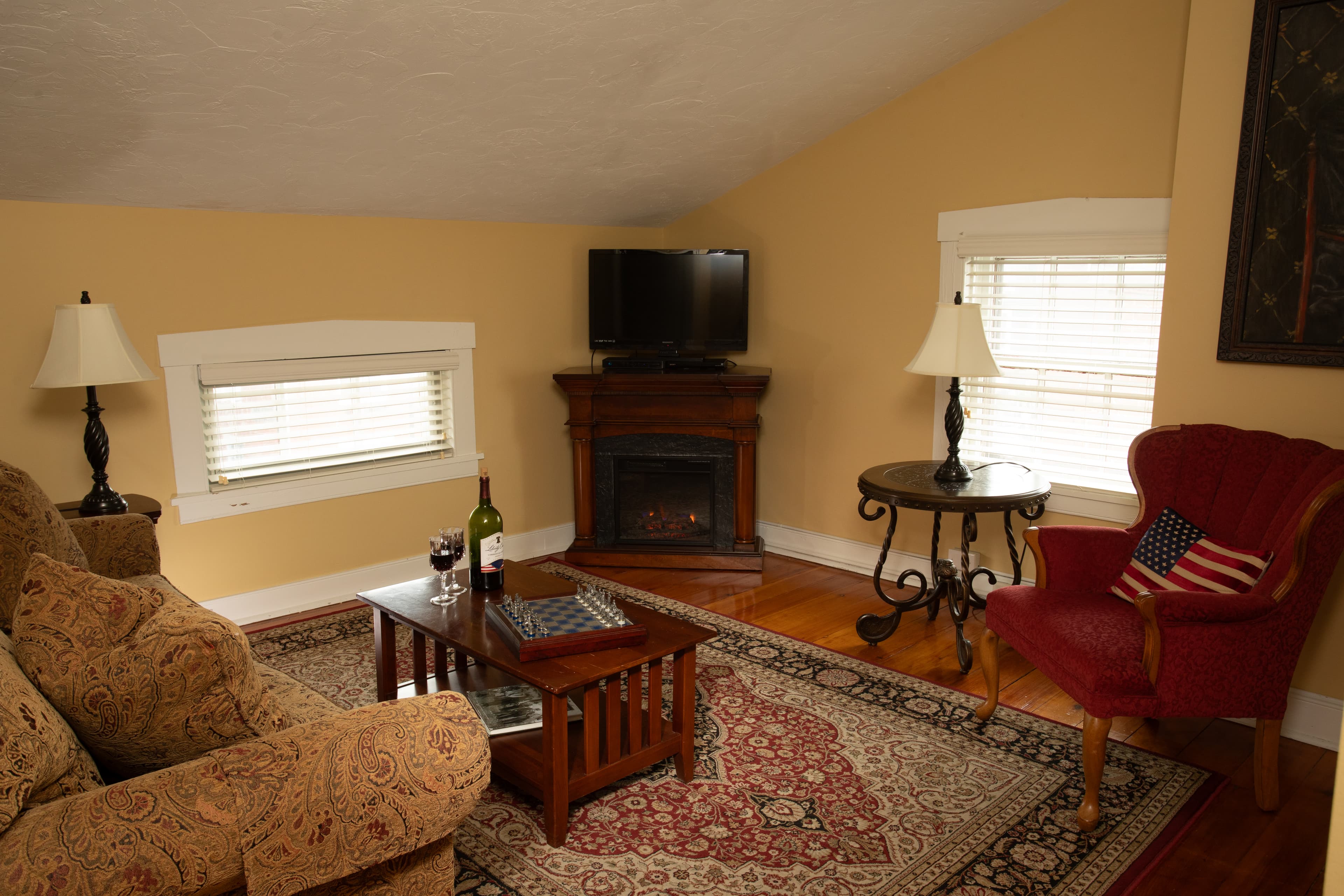 The Lincoln Suite also features a sitting room with a sleeper sofa, a chair, an electric fireplace, TV, and original wooden floors with an area rug.