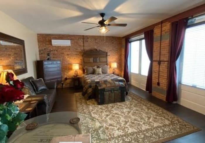 The Carriage House Suite is a ground-level room located in our detatched carriage house.  This room features vinyl plank floors, area rug, a queen size bed with a Victorian head board, 2 night stands with lamps, a leather sofa, a high boy dresser, electric fireplace, a whiskey barrel table, and a split HVAC unit.  This room also has a small refrigerator and a coffee maker.