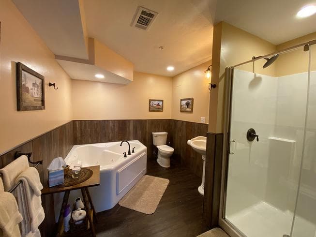 The Carriage House bathroom includes a pedestal sink, jetted tub, toilet, and a walk in shower.