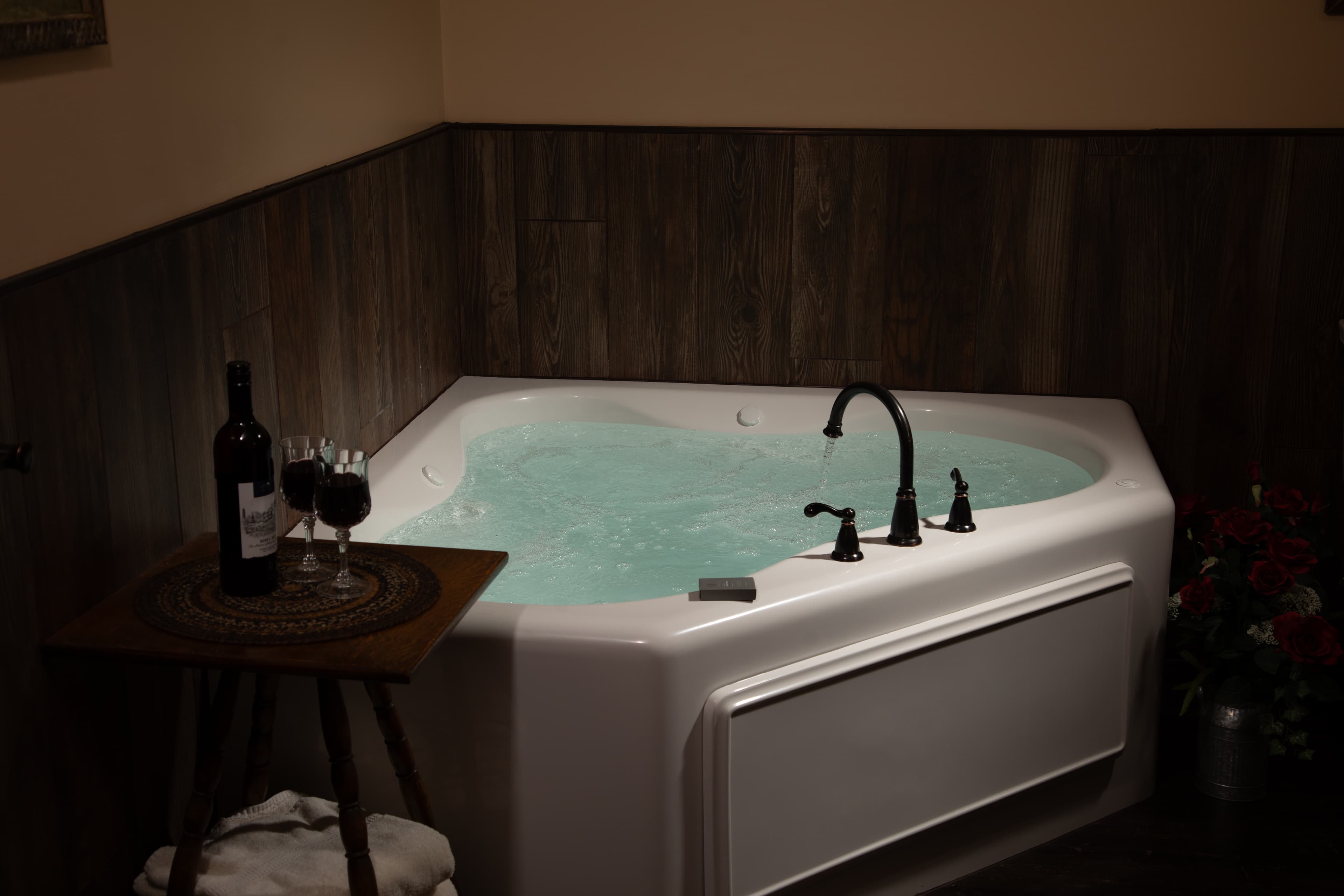 A cozy corner in the Carriage House featuring a heart-shaped hot tub next to a bottle of wine and two glasses.