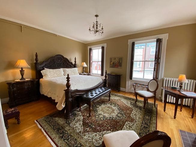 The Miss Dorothy Suite features a Grand King size wooden bed with a  white quilted covering.  This room also has 2 night stands with lamps, a table and 2 chairs in the main bedroom, wooden floors, with area rugs, and an electric fireplace.