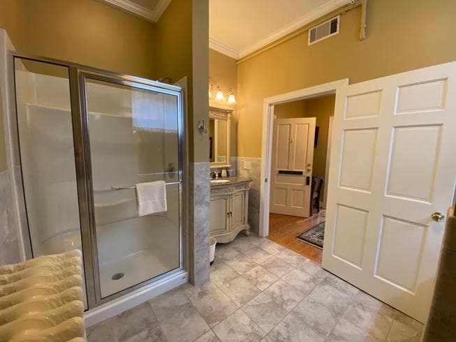 The Miss Dorothy Suite bathroom features tile floors, an ornate wooden sink with marble top, walk in shower, toilet, and a jeted tub for 2.
