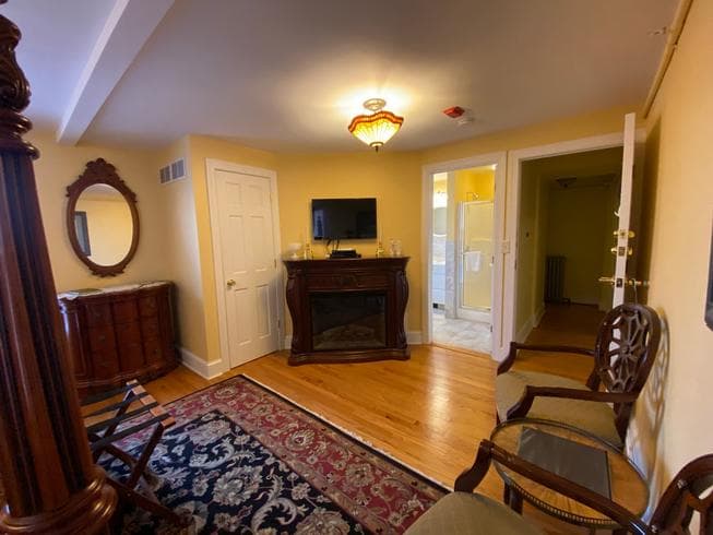 The Colonel Chamberlain Suite features a dresser, 2 chairs, electric fireplace, and TV.
