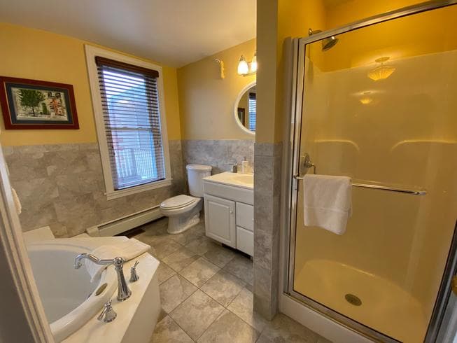 The Colonel Chamberlain Suite bathroom features a walk in shower, large soaking tub, sink, toilet, and tile flooring.