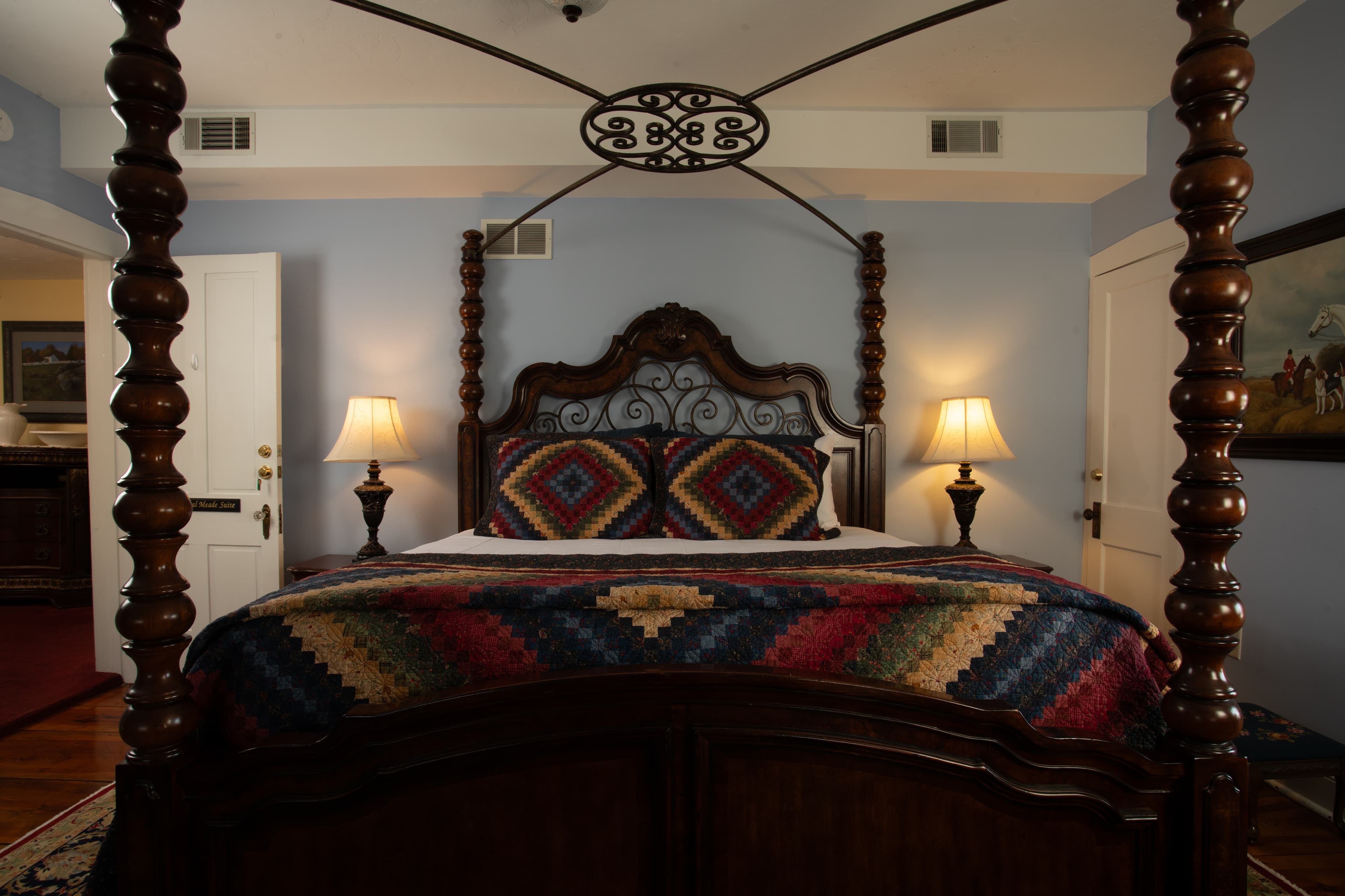 A beautifully decorated bedroom featuring a four-poster bed with a vibrant quilt and warm lighting.