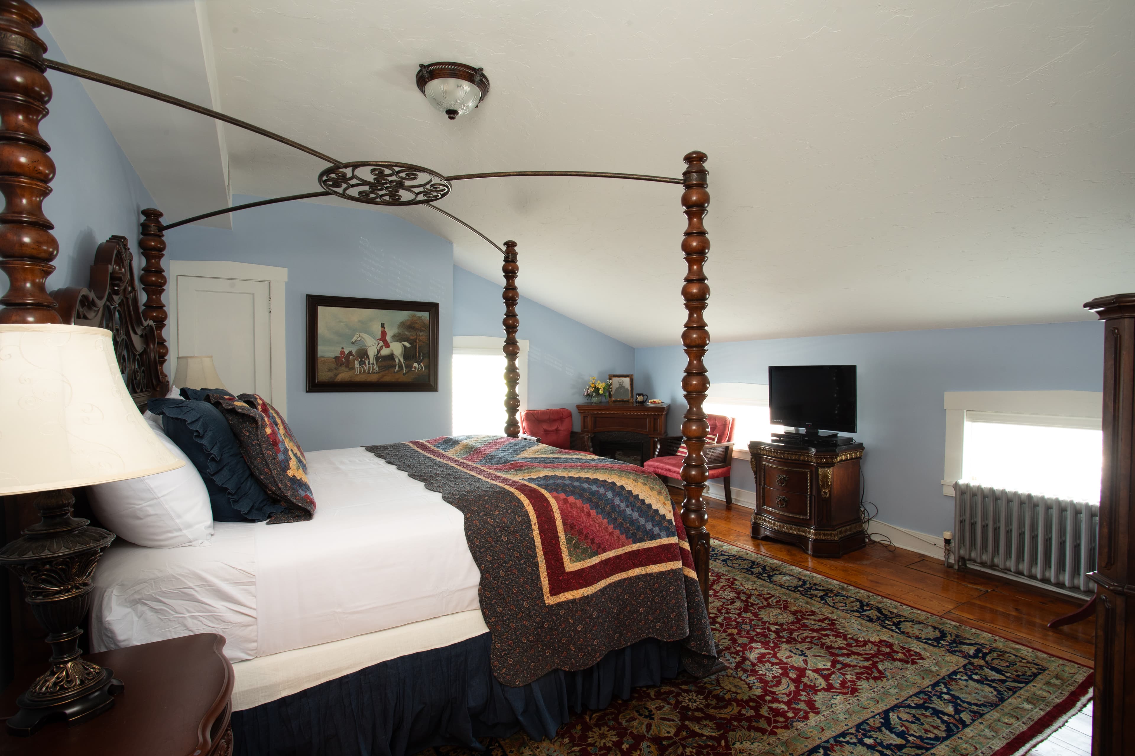 A cozy bedroom featuring a four-poster bed, a TV, and a vintage rug.
