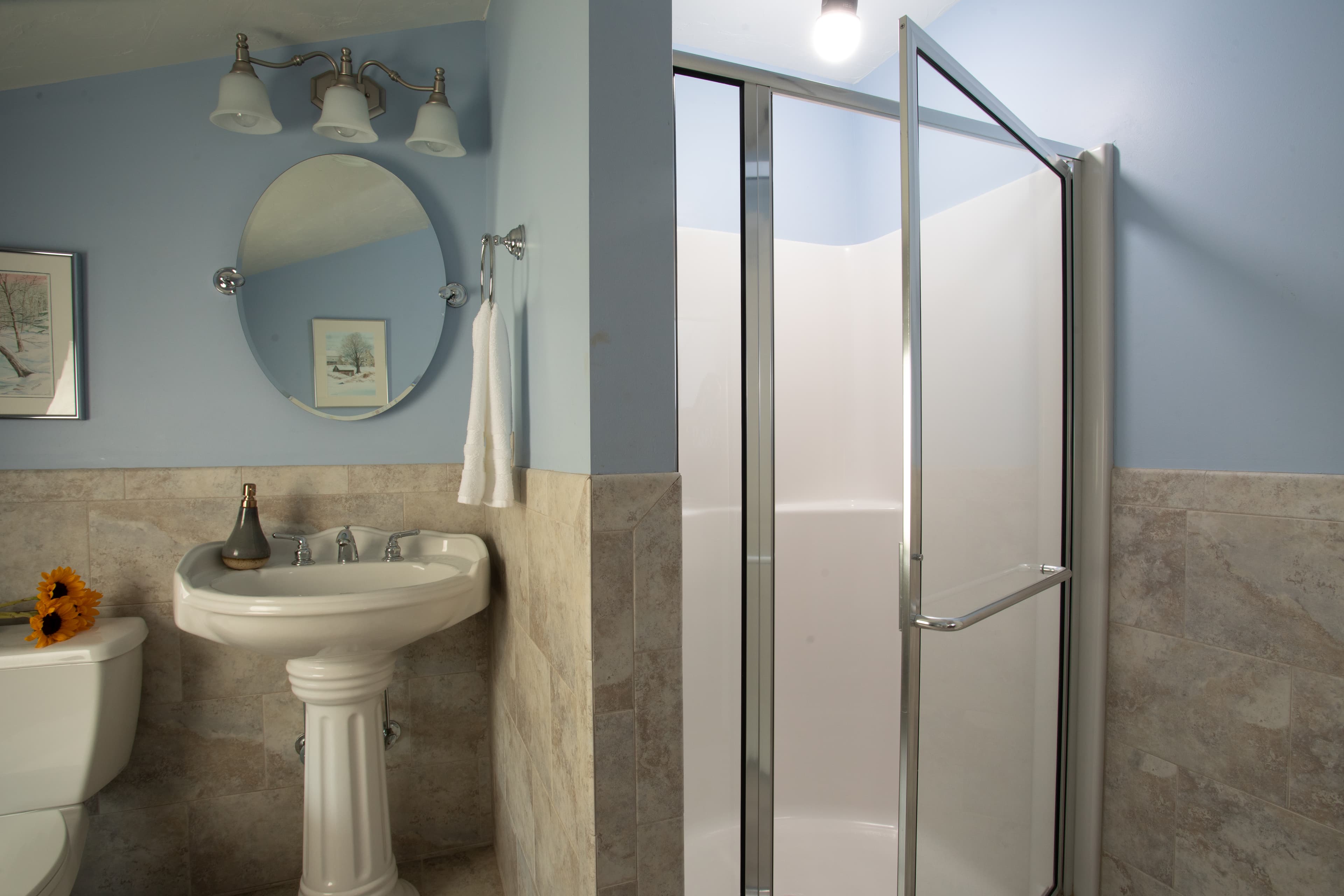 A light blue bathroom features a pedestal sink, modern mirror, and a glass shower enclosure.