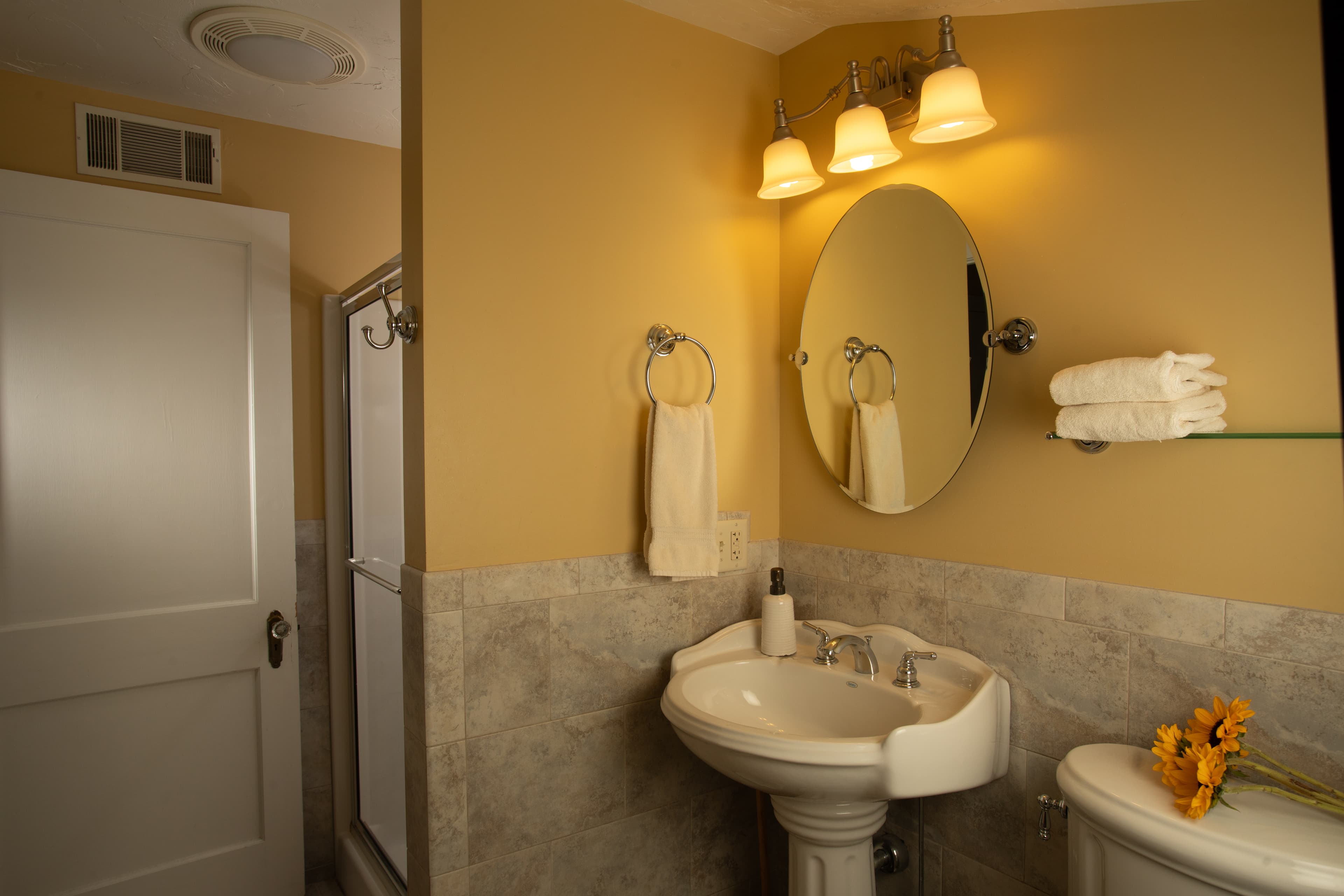 A cozy bathroom featuring a pedestal sink, mirror, and warm lighting.