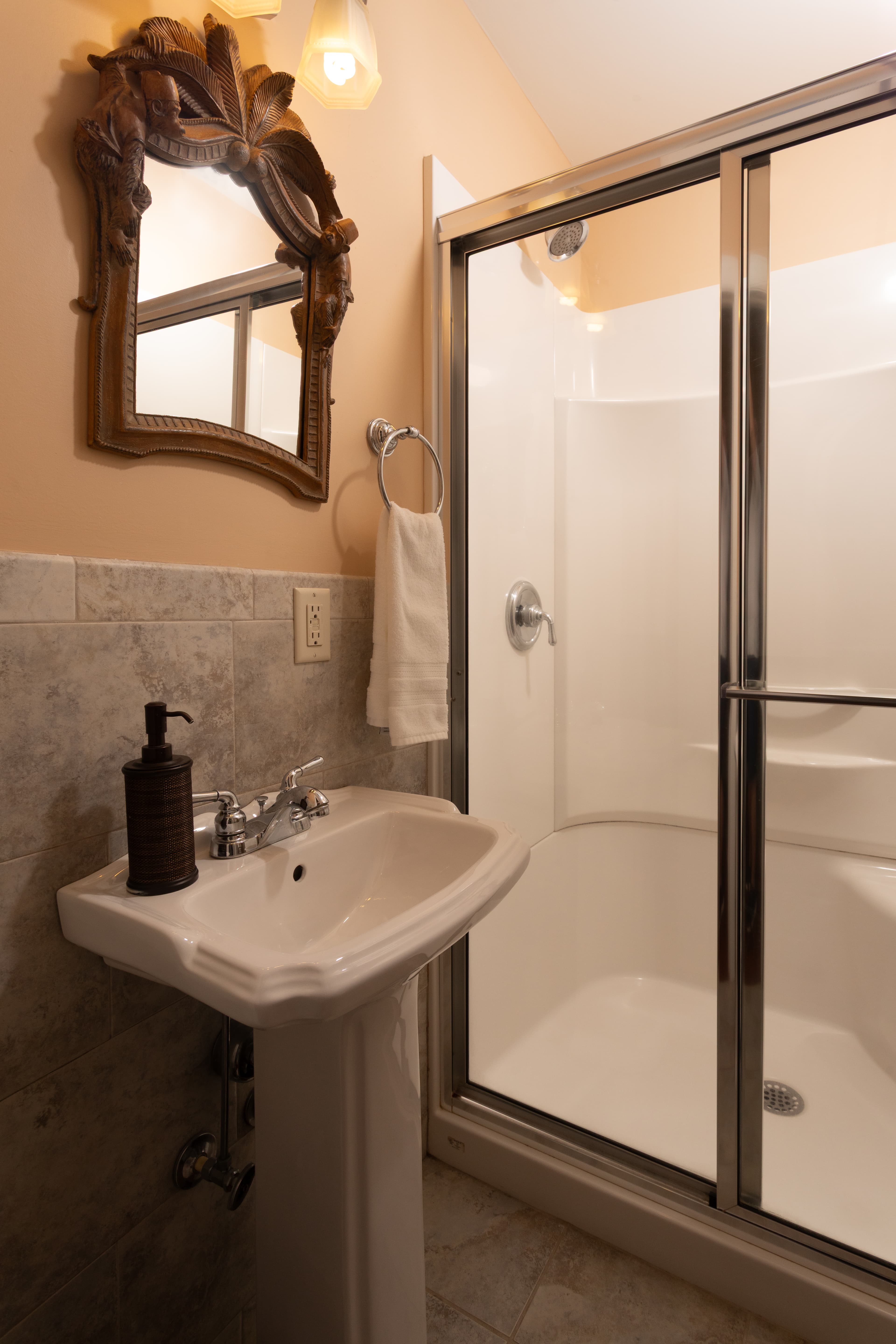 A compact bathroom featuring a pedestal sink, a shower stall with glass doors, and a decorative mirror.