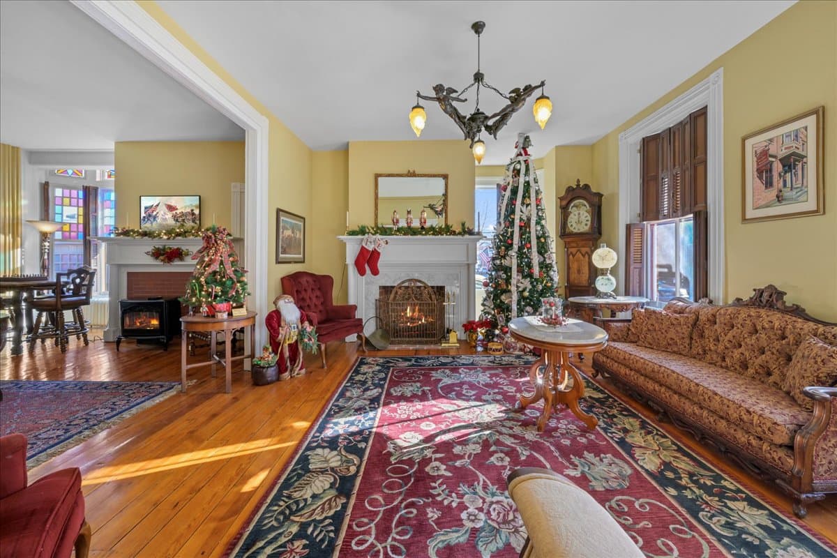 A cozy living room decorated for the holidays, featuring a Christmas tree, fireplace, and elegant furnishings.