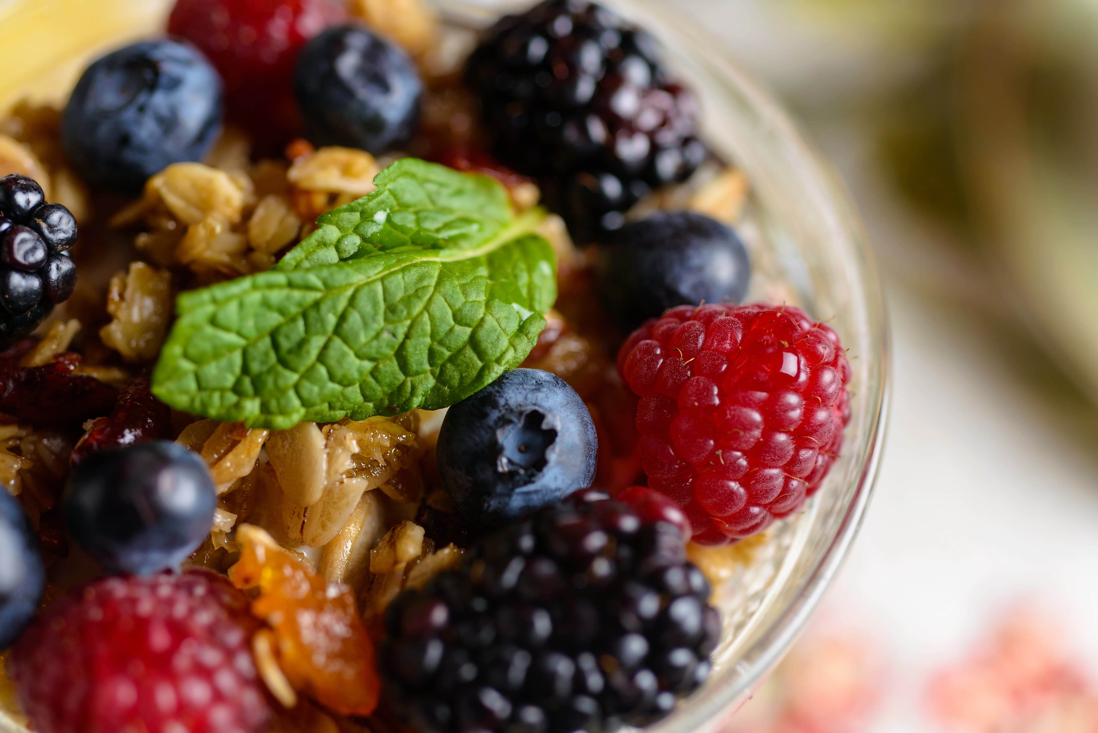 A close-up of a parfait with layers of granola, mixed berries, and a sprig of mint.