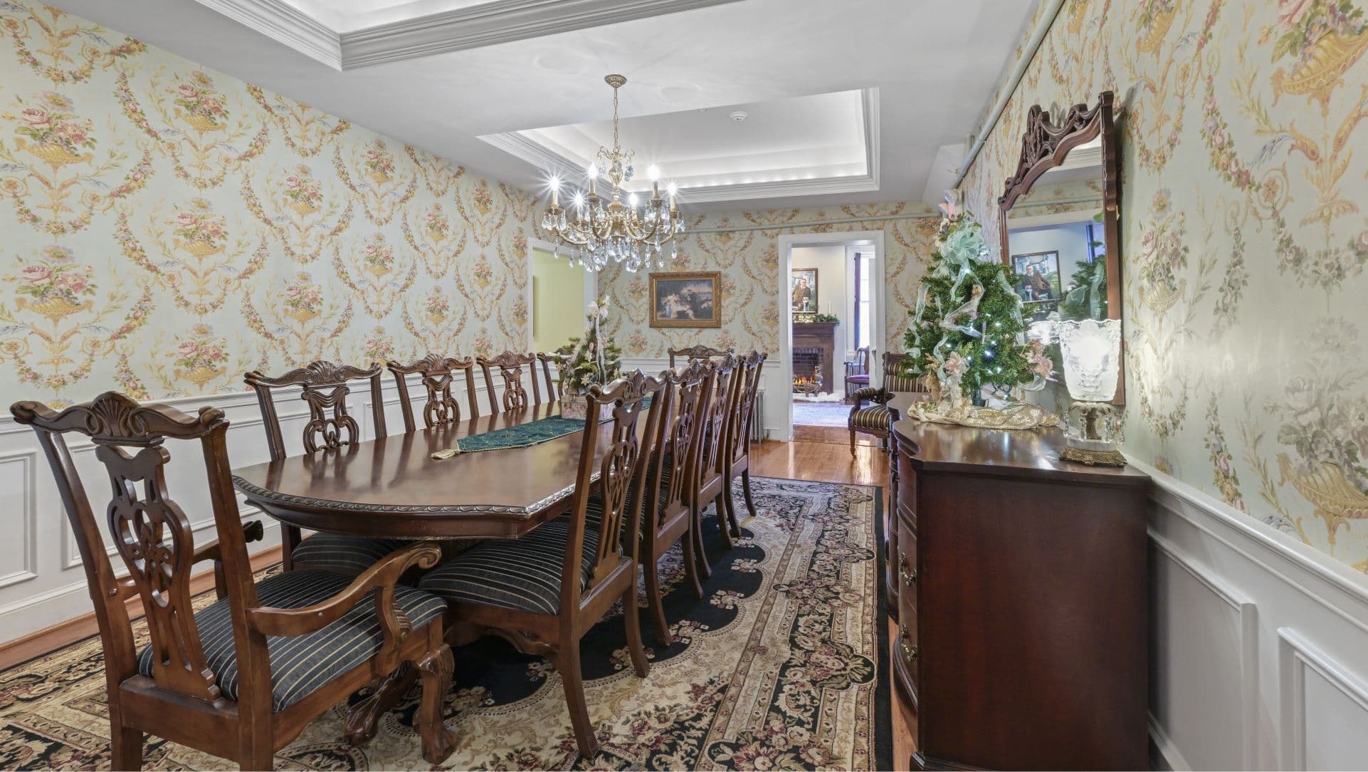 A spacious dining room with a long wooden table, elegant chairs, and ornate wallpaper.